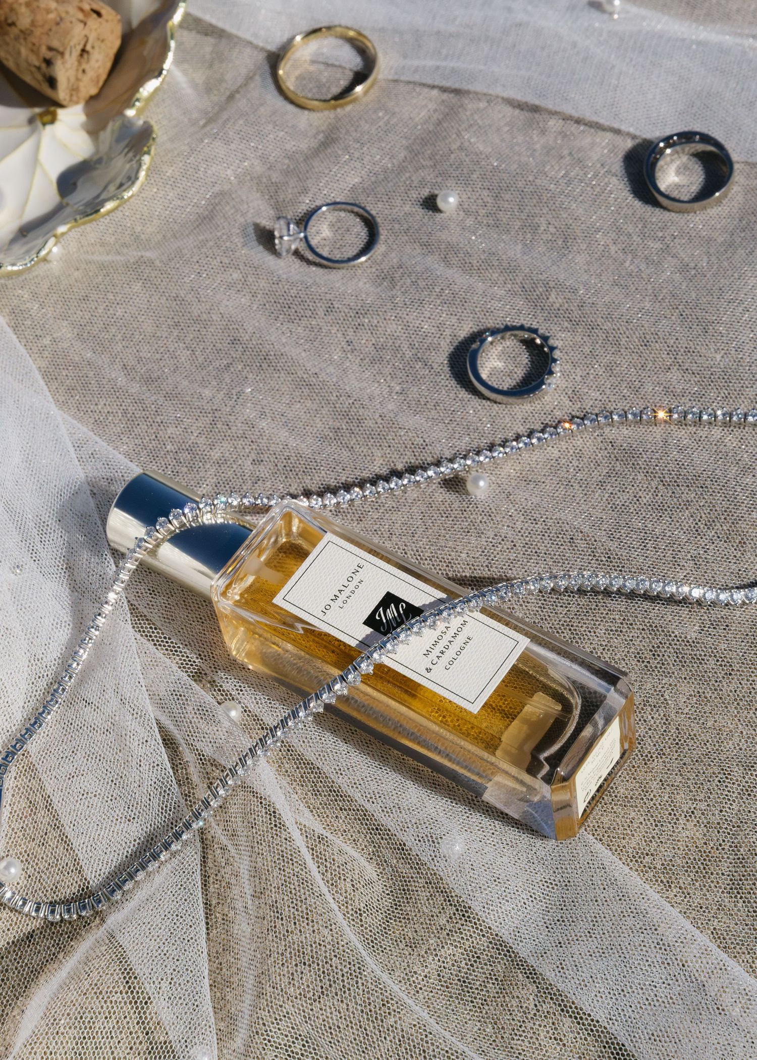 Luxury perfume bottle with silver chain necklace displayed on textured gray fabric.