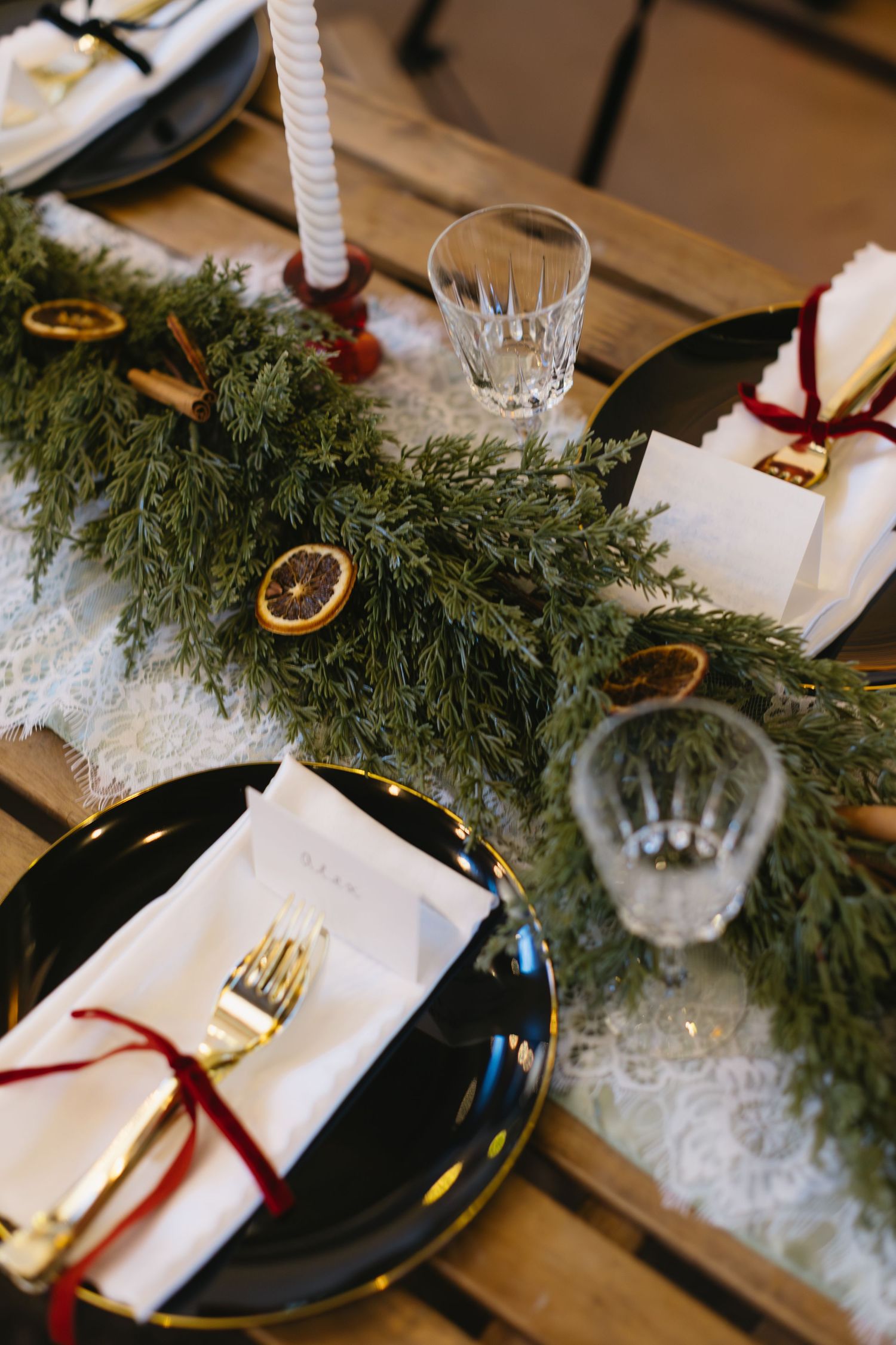 Wedding table settings with evergreen garland, white candles, and black plates.