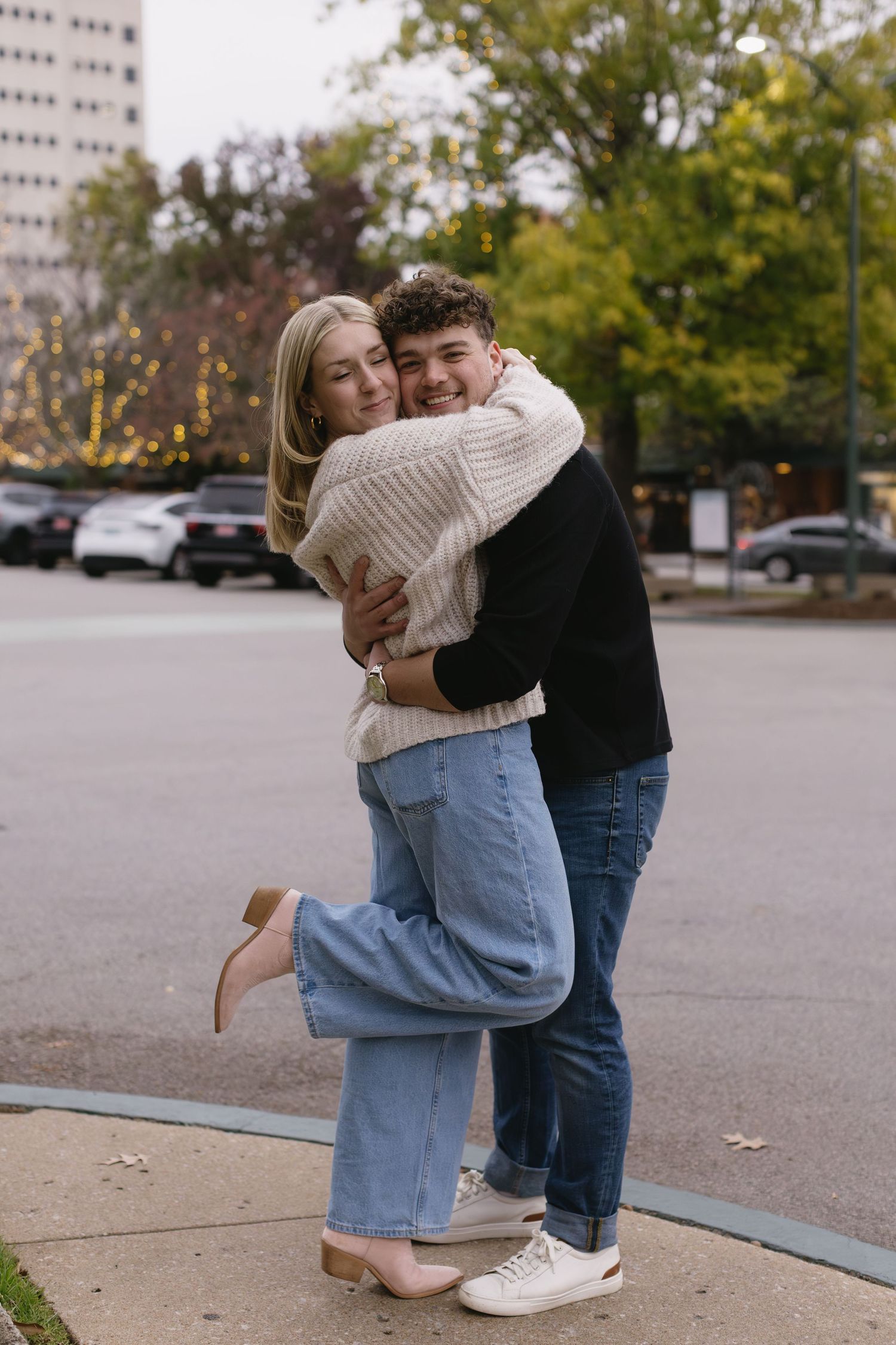 A joyful embrace between a couple on a city sidewalk wearing coordinated casual outfits.