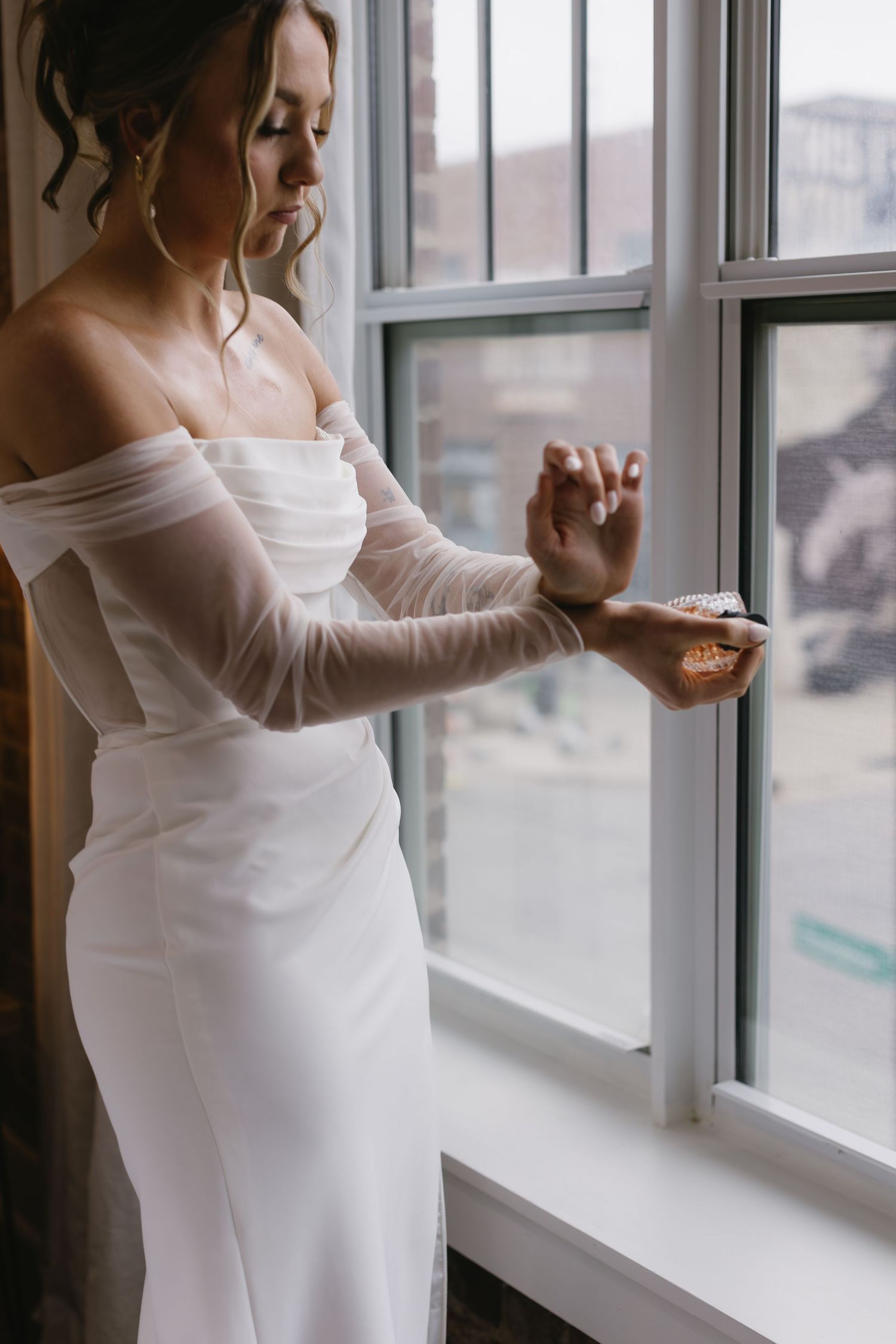 Elegant white maternity wedding dress shown in window light with off-shoulder neckline detail.