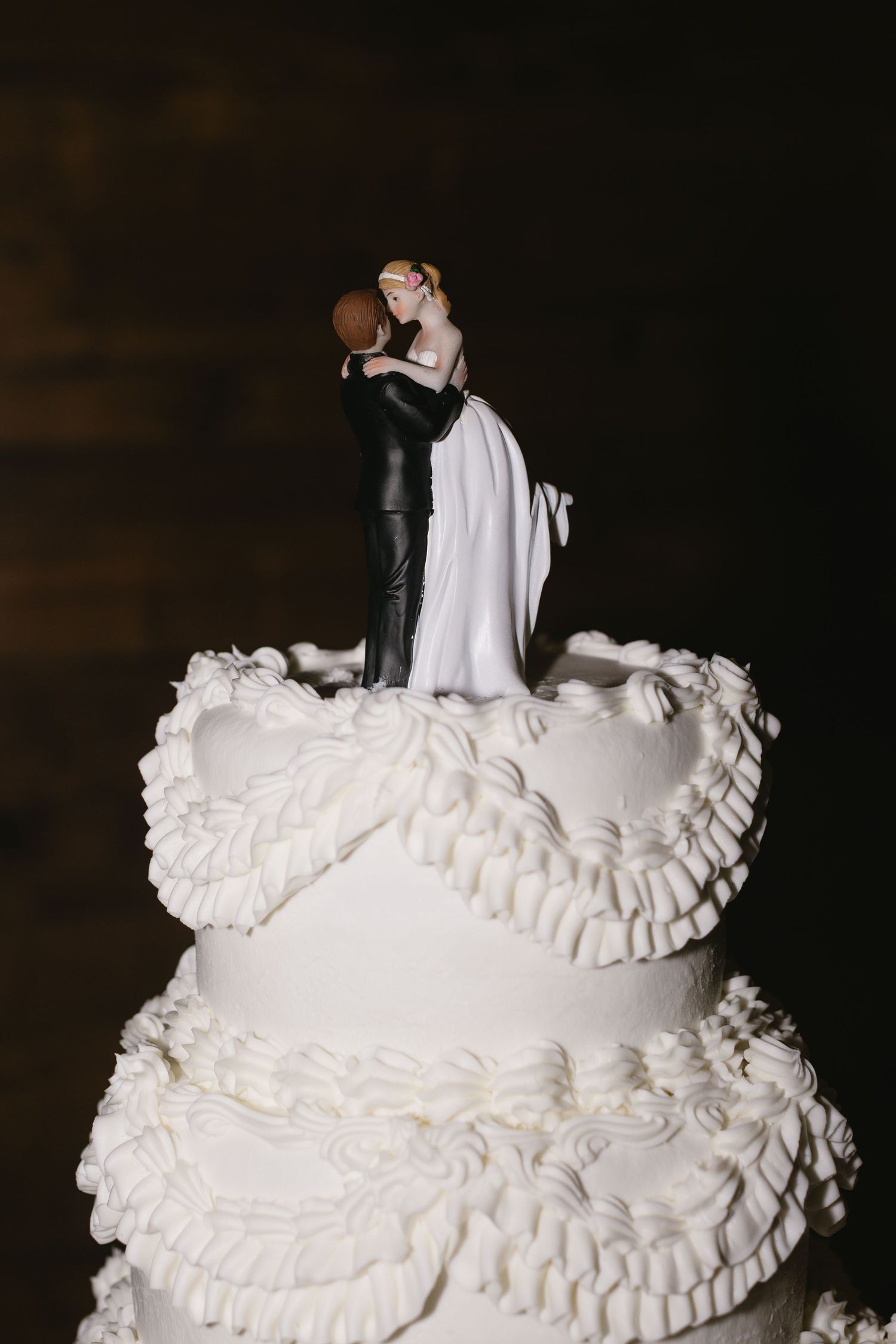 Close-up of an elegant white wedding cake with ruffled tiers and a traditional topper.