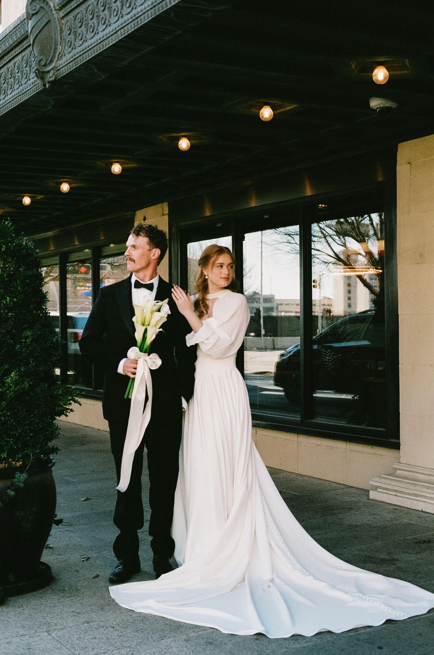 Wedding couple poses under covered walkway with dramatic train of white dress flowing.