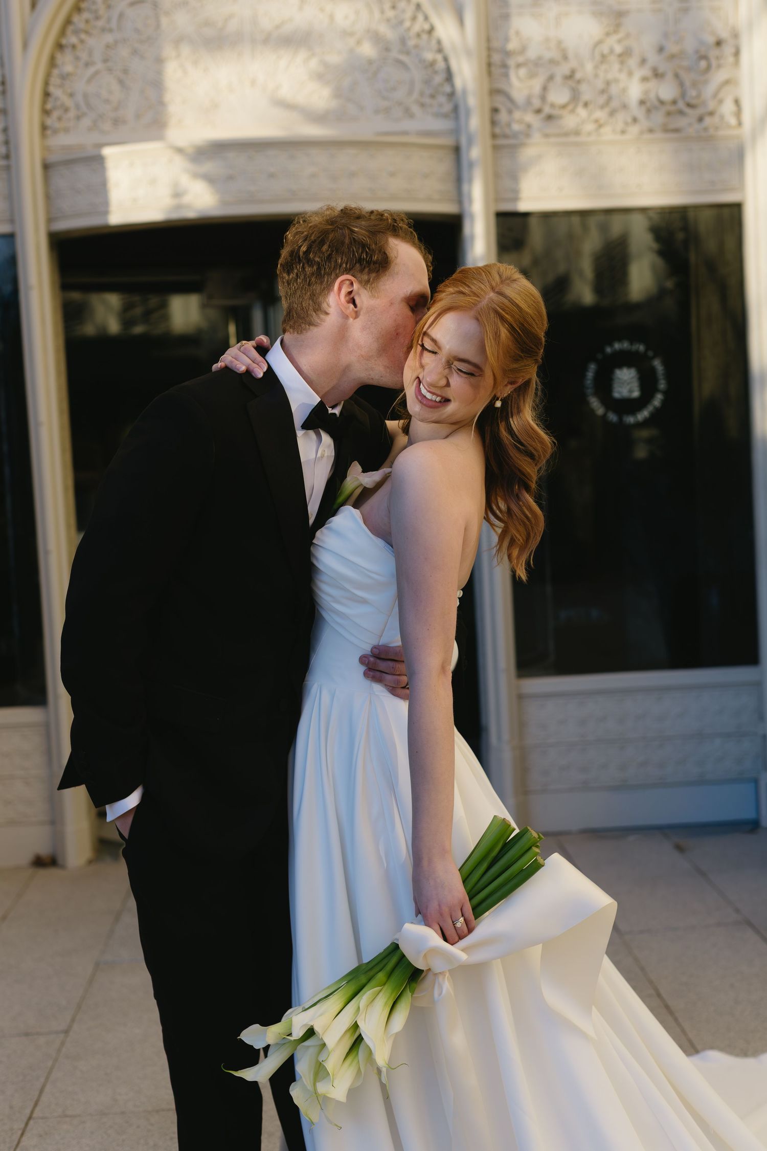 Sunlit outdoor wedding portrait showing tender moment between newlyweds.