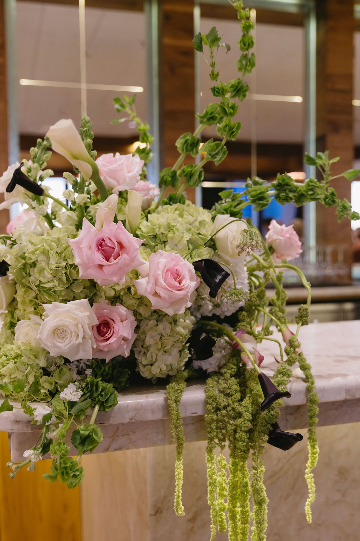 Elegant floral centerpieces with pink roses and cascading greenery line a reception table.
