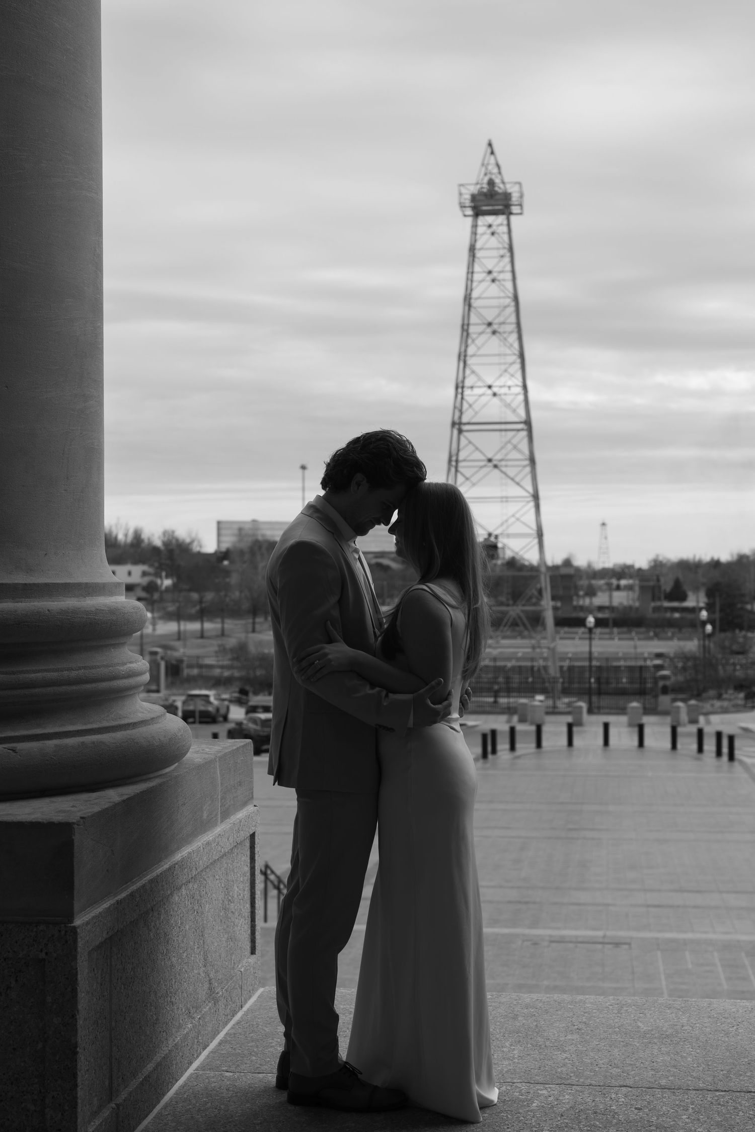 A silhouetted couple embraces near a column with an industrial tower visible in the background.