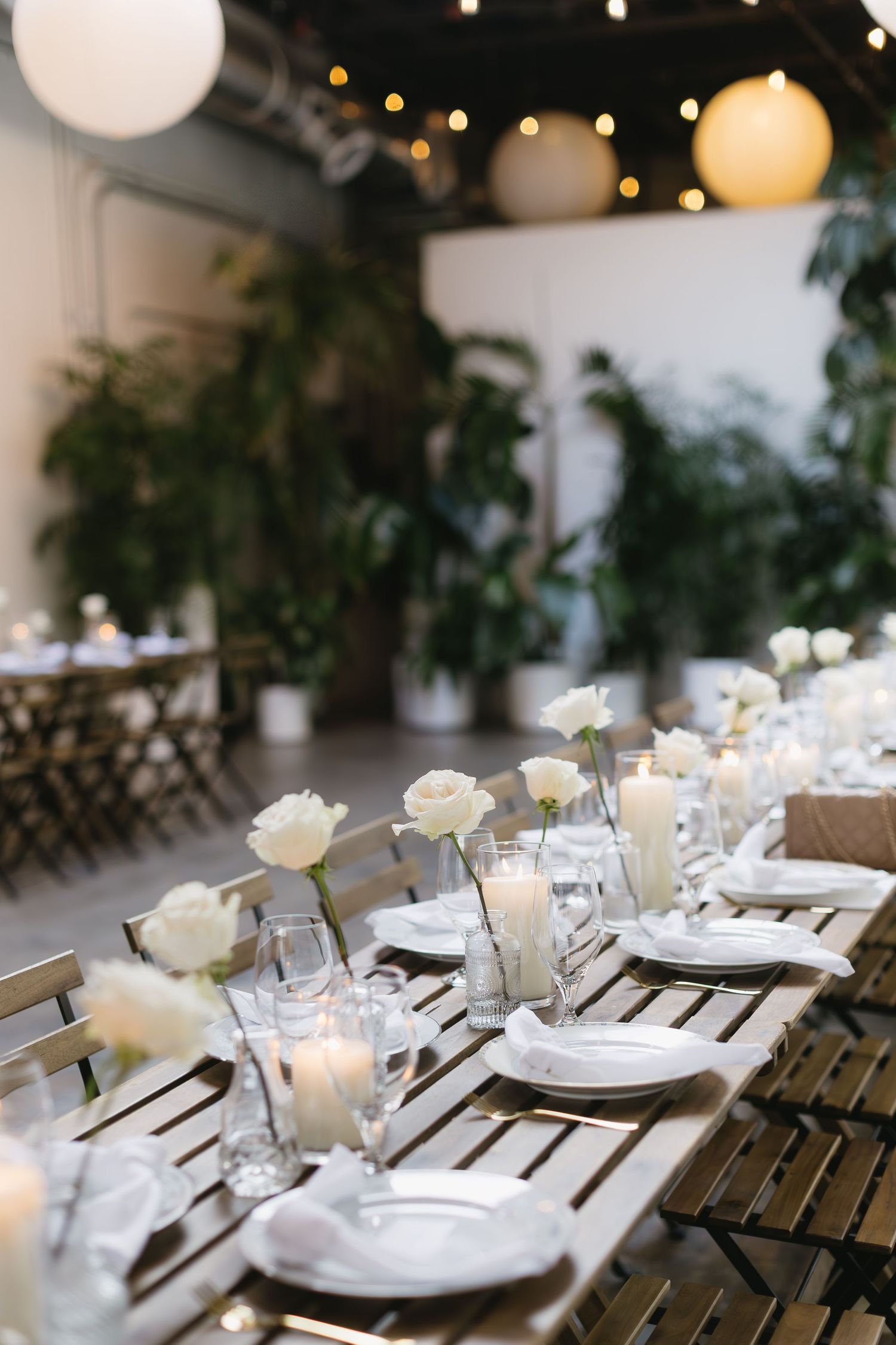 White china place settings with candlelight and floral centerpieces adorn rustic wooden tables at an elegant wedding reception.