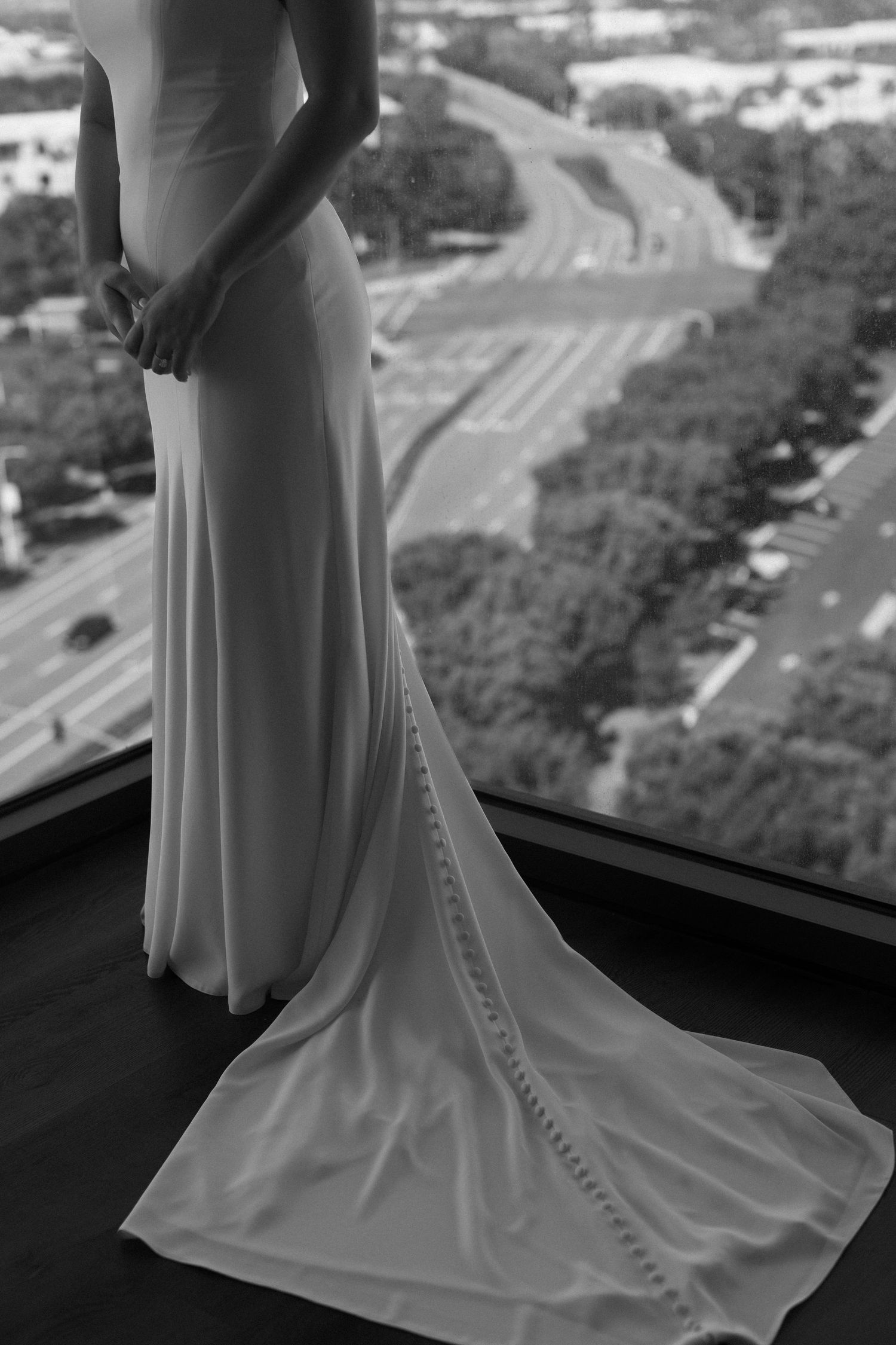 Close-up details of an elegant white wedding dress train with delicate buttons and flowing fabric against a cityscape backdrop.