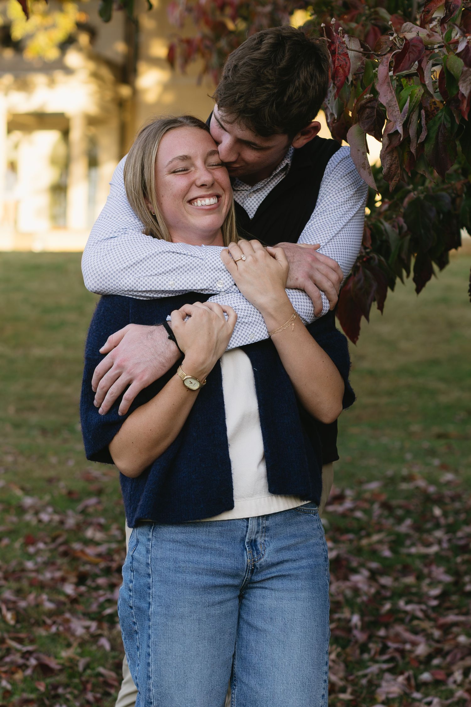 Couple embracing among autumn leaves with golden sunlight filtering through.