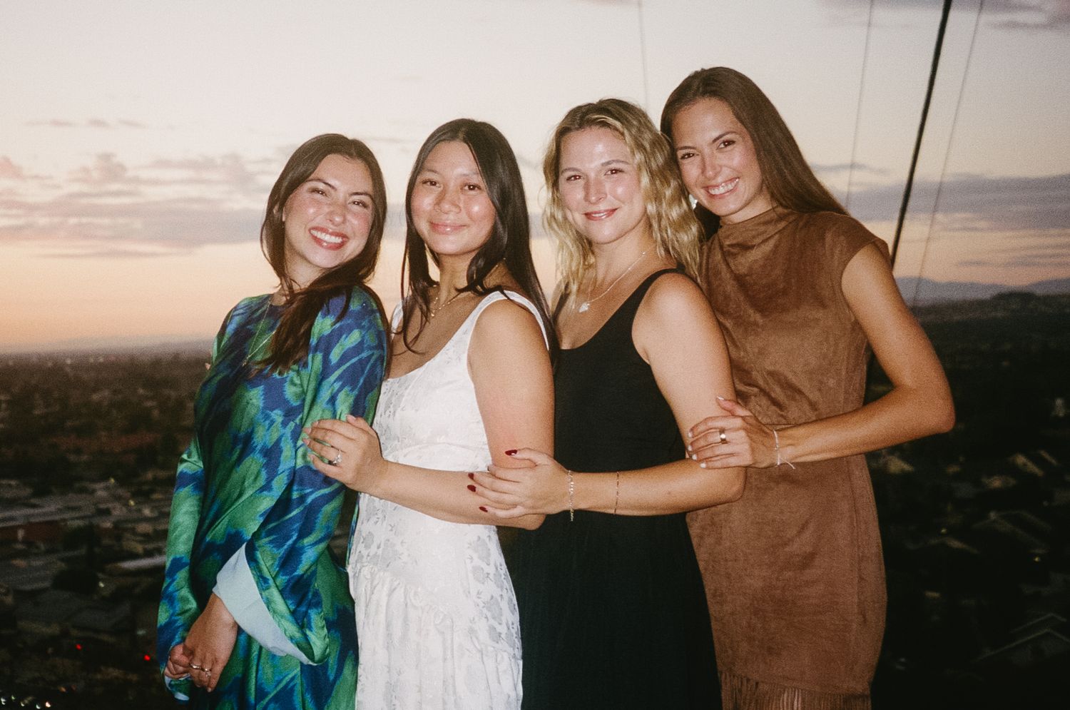 Group of friends laughing and embracing while standing together at sunset on a beach.