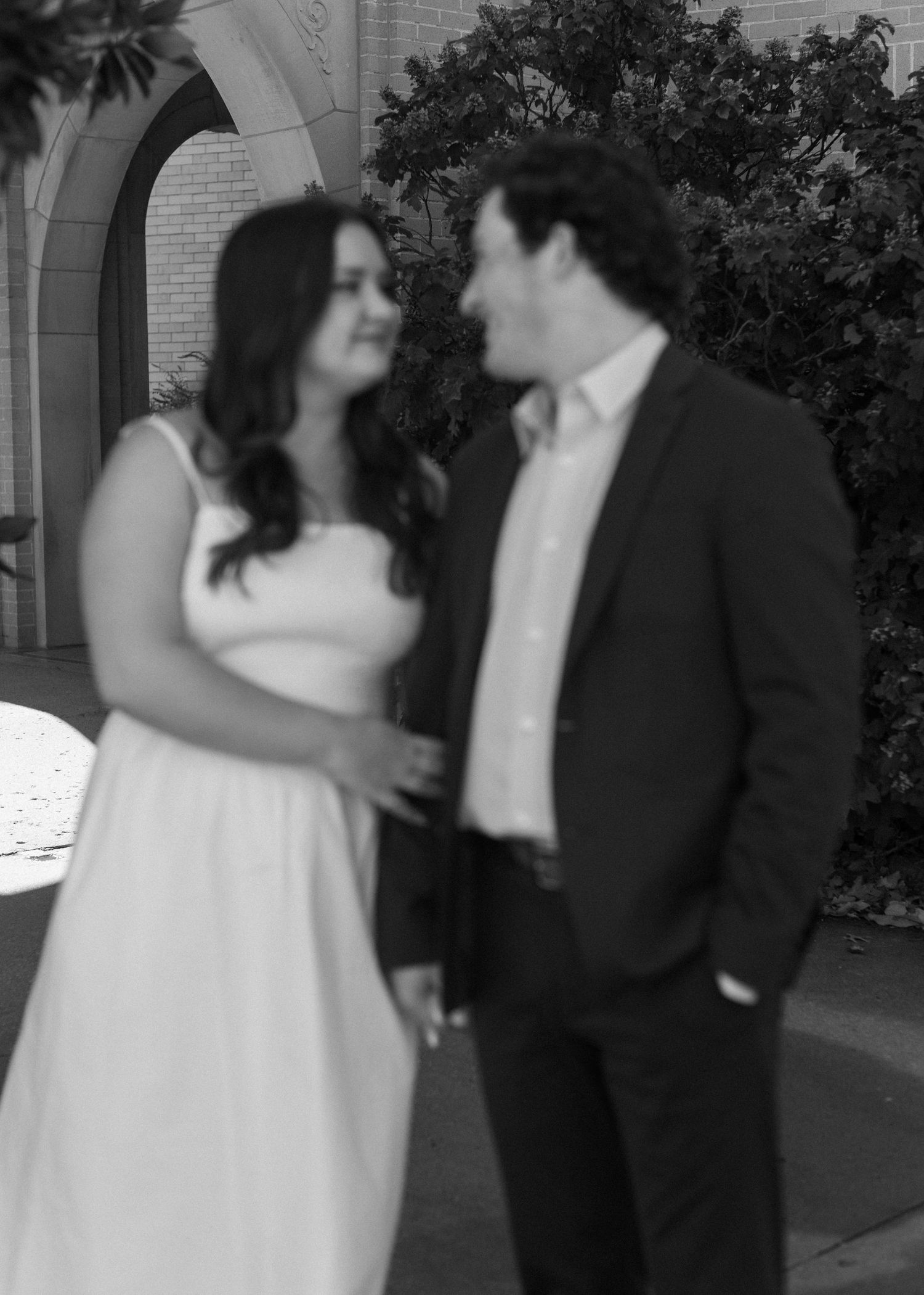 A romantic black and white photo of a couple in formal attire gazing at each other outdoors.