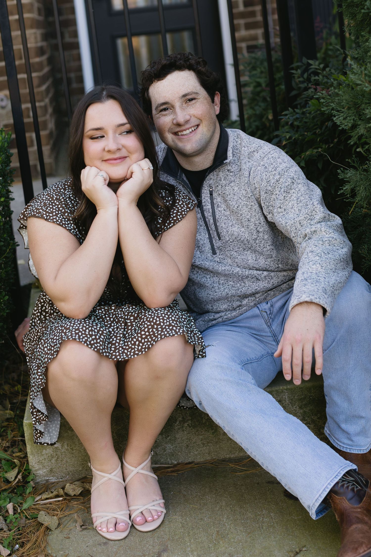 A couple sits together on concrete steps near a brick building.