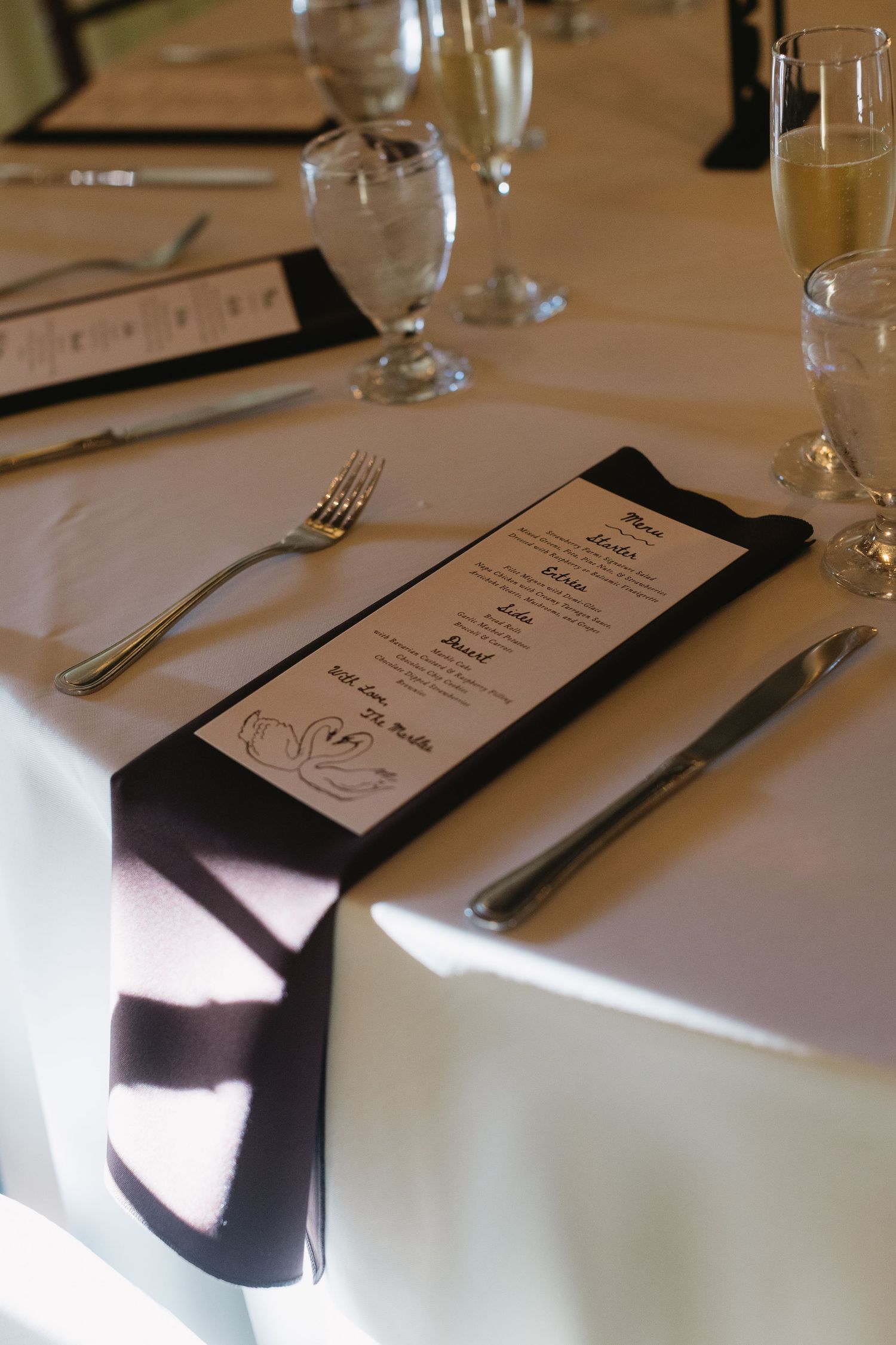 Elegant place settings with menus and silverware arranged on white tablecloths at a wedding reception.