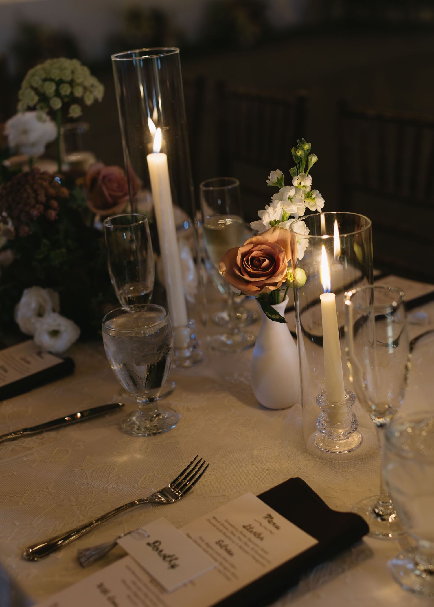 Elegant table setting with lit candles, wine glasses and menu cards at a wedding reception.