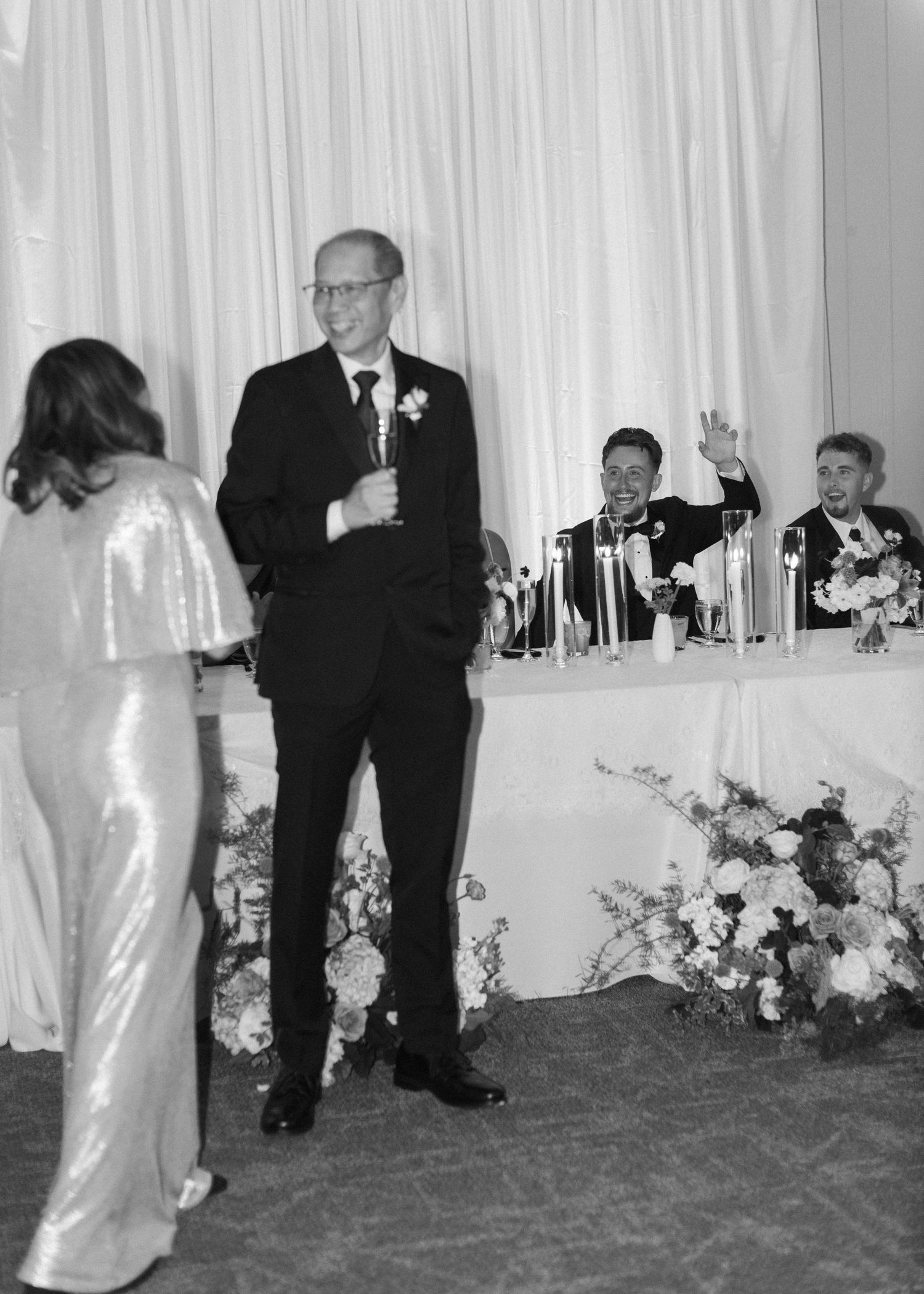 Elegant wedding reception setup with white draping and floral arrangements along the head table.