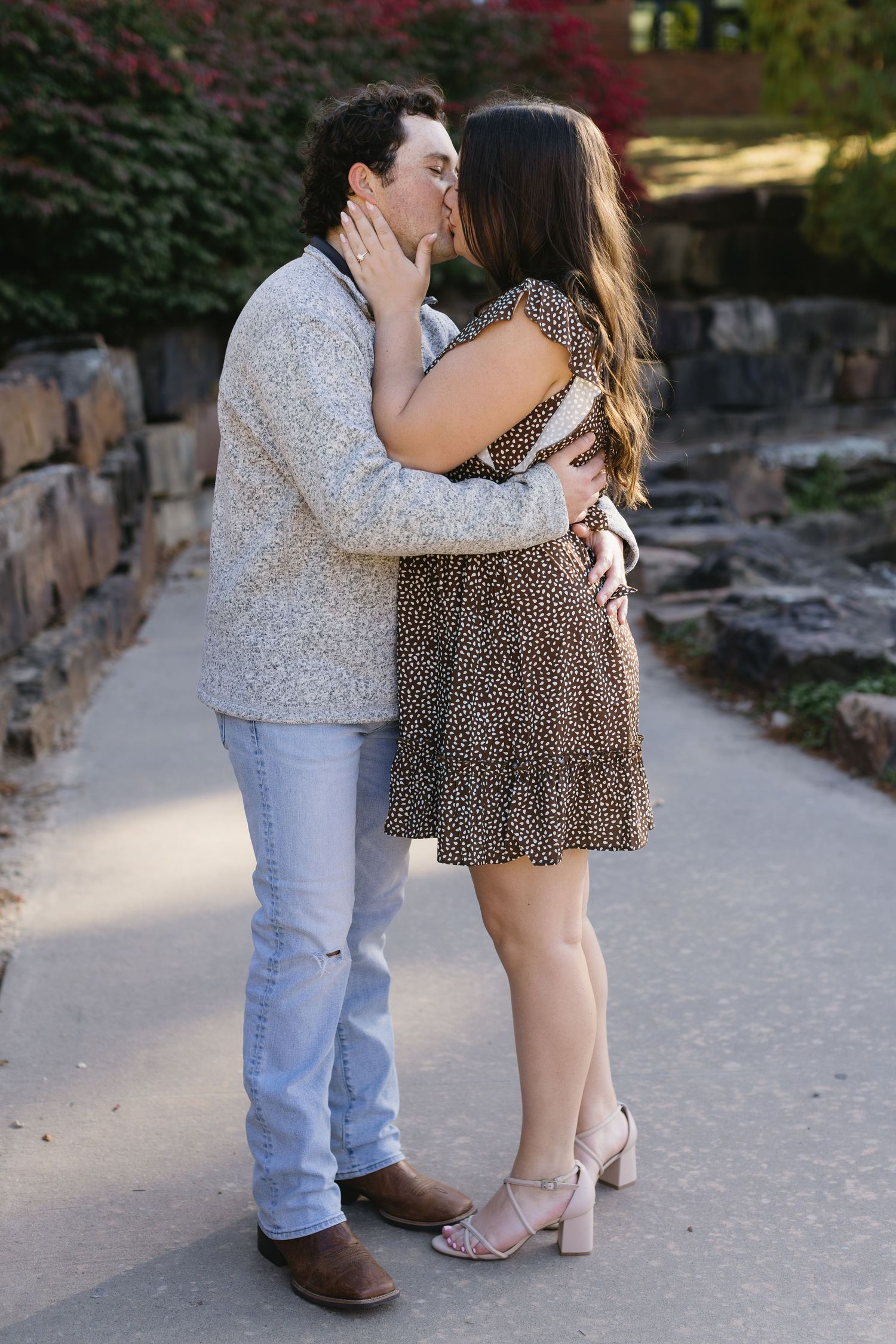A romantic couple shares a tender kiss on a pathway, wearing casual autumn attire.