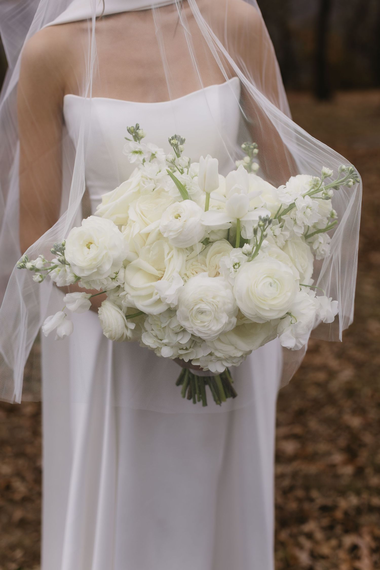 Close-up of white rose bridal bouquet with delicate veil in natural outdoor setting.