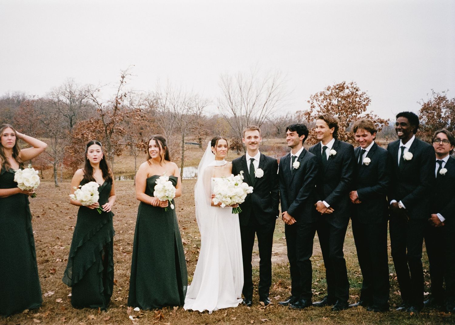 A wedding party poses for a panoramic photo in formal black and white attire.