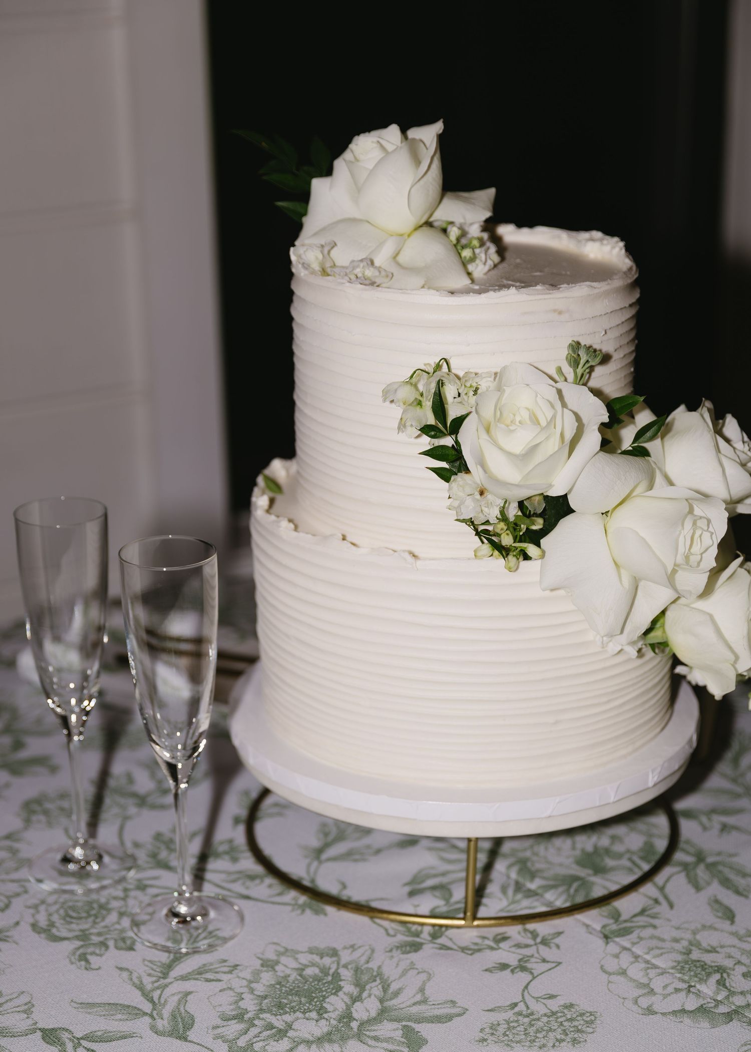 An elegant two-tier white wedding cake decorated with fresh white roses and greenery.