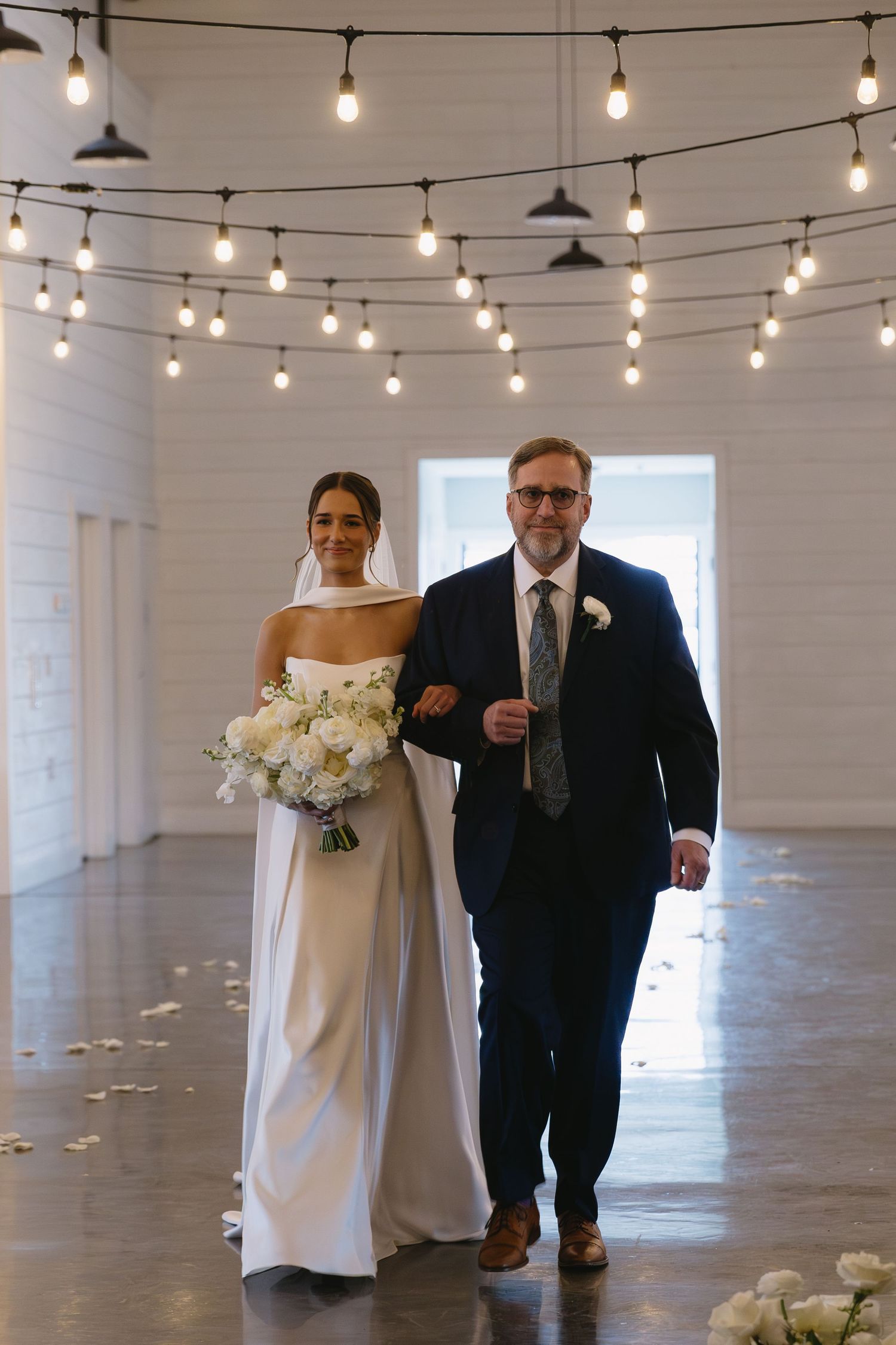 Elegant wedding ceremony space with string lights hanging from white industrial ceiling.