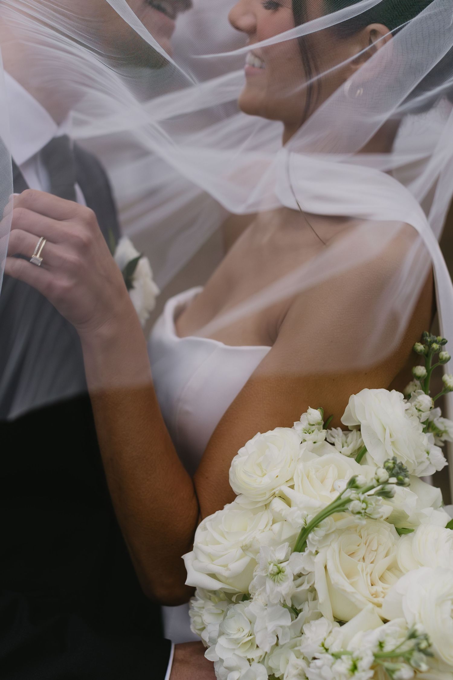 Close-up of elegant white rose bridal bouquet with flowing veil in background.