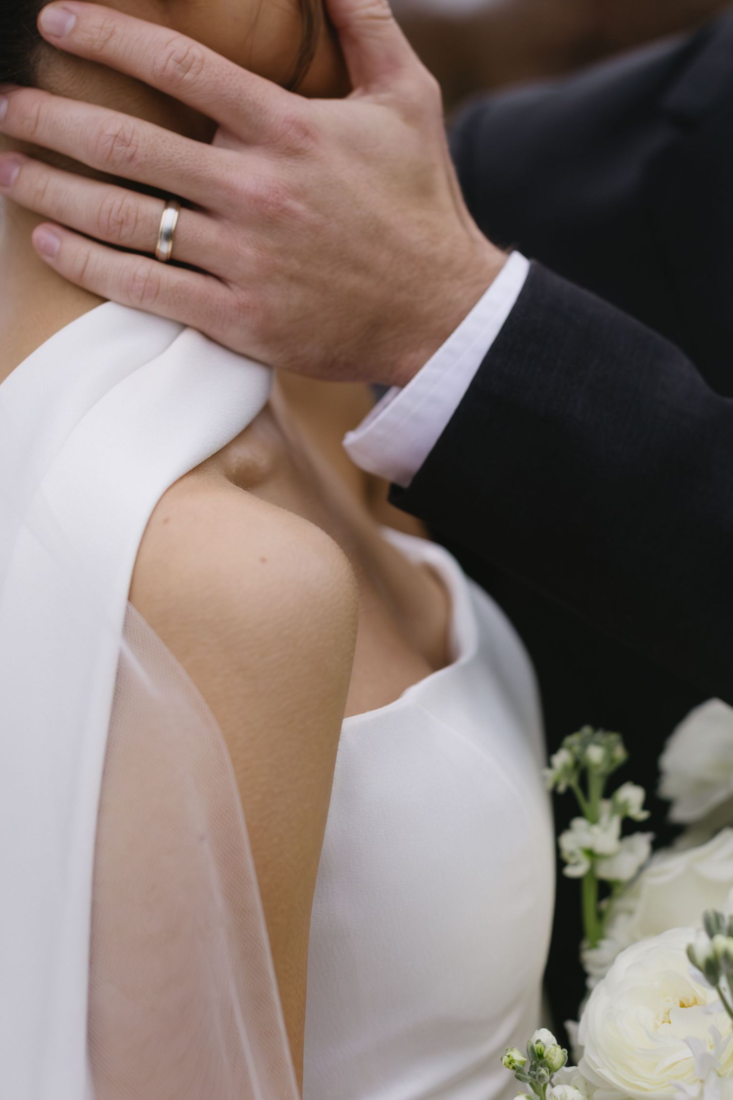 Close-up detail of hands and white wedding dress with delicate floral bouquet.