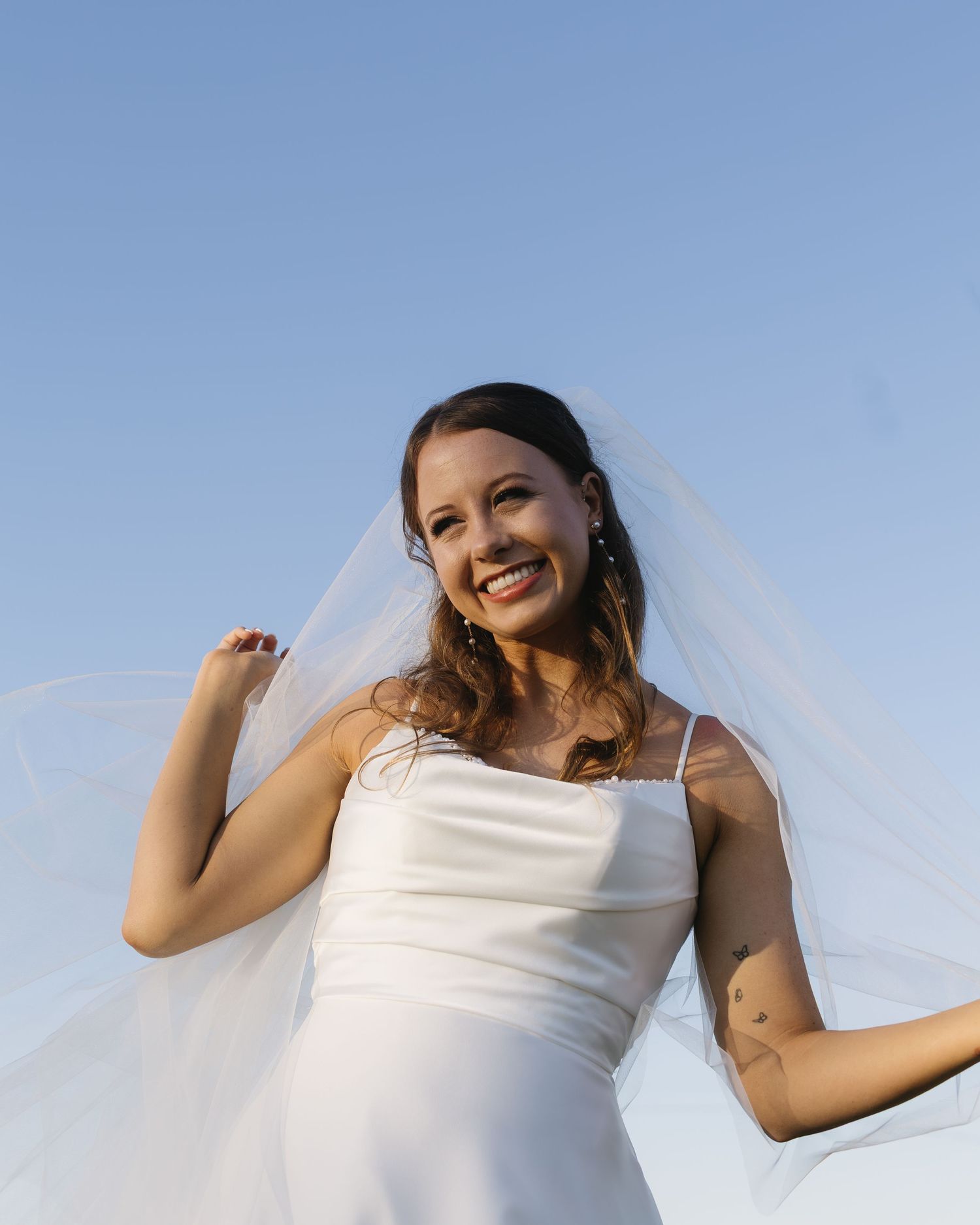Low-angle shots of a bride against blue sky wearing a simple white wedding dress.