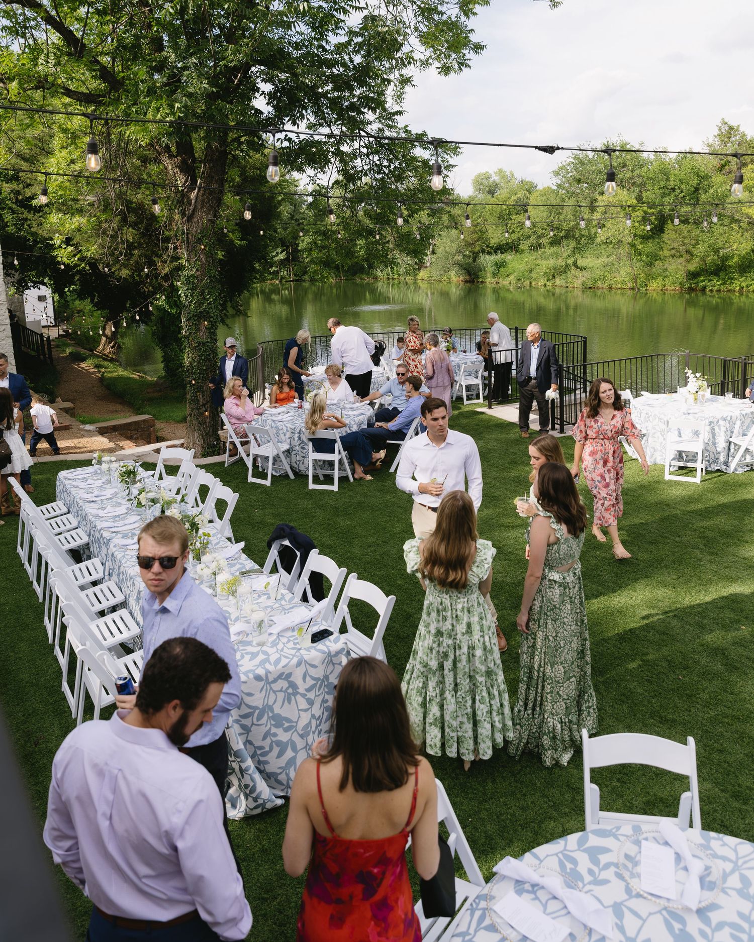 Garden wedding reception setup with long white tables and chairs arranged outdoors near a pond.