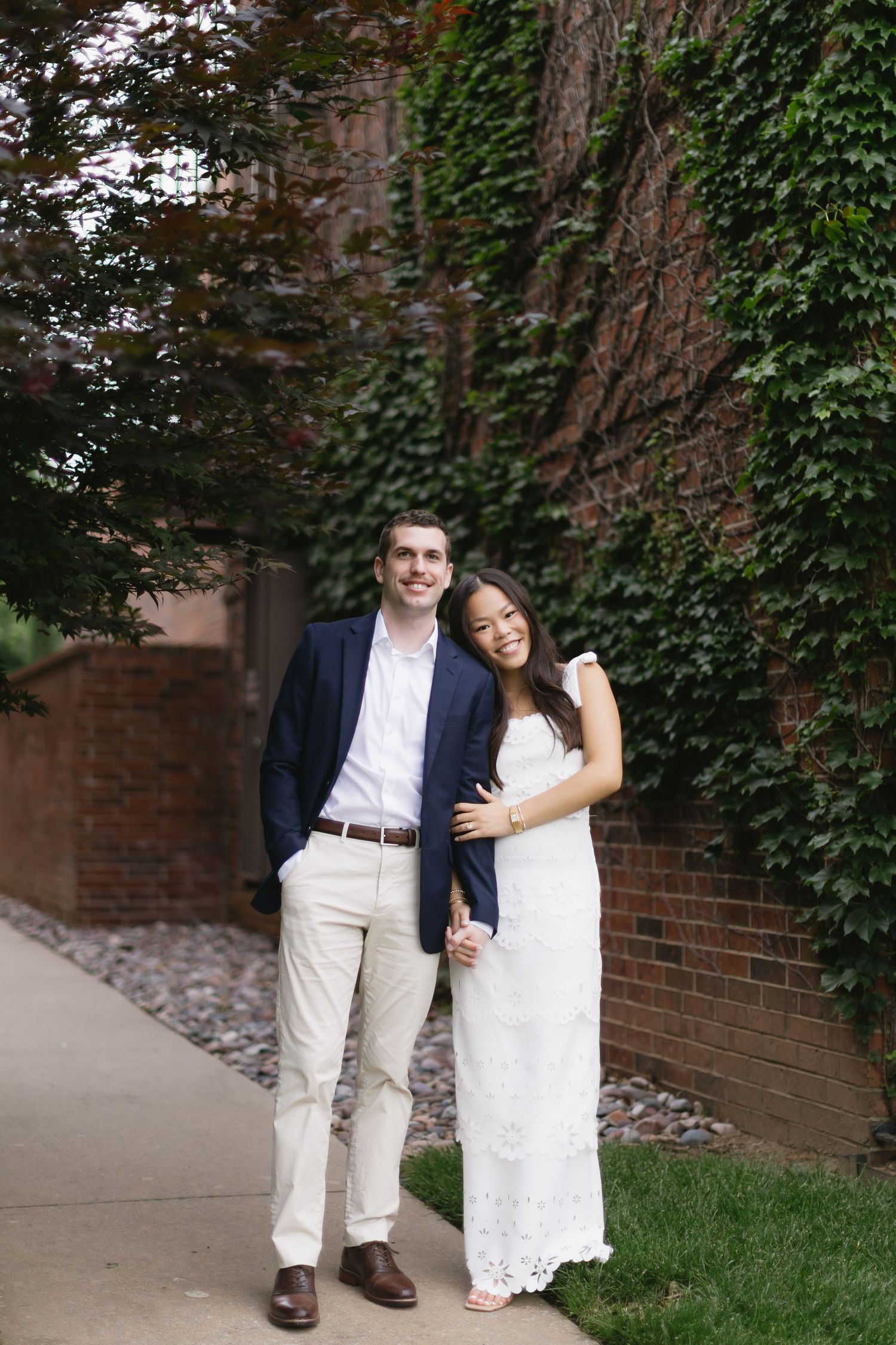 Couple laughs together against ivy-covered brick wall during photo session.