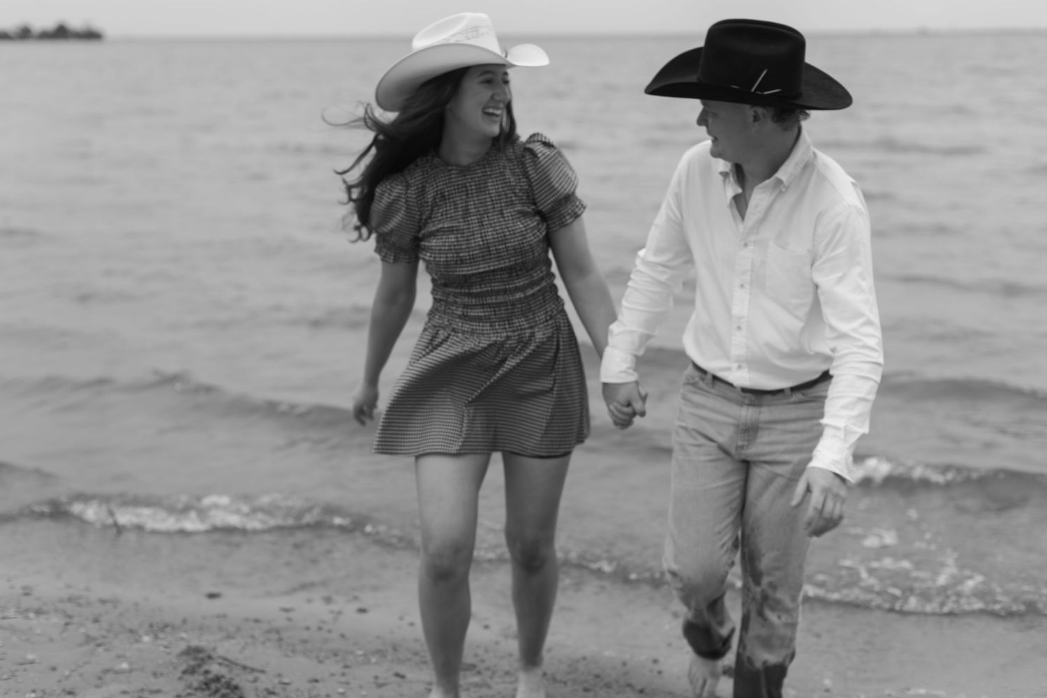 Coastal engagement photoshoot with couple walking by the water's edge.
