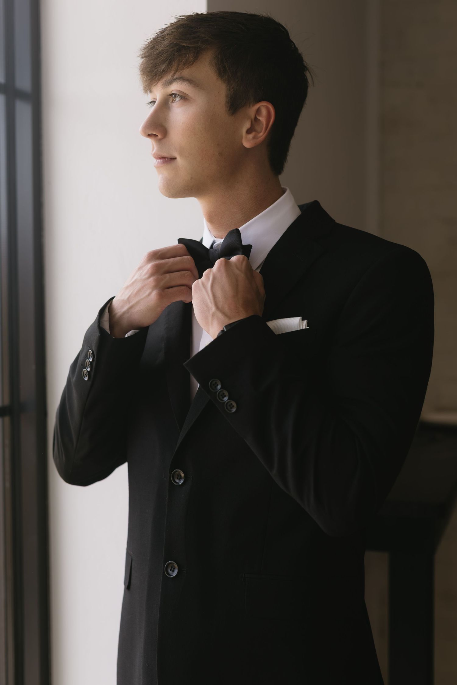 Person in formal black suit adjusting collar in moody lighting.