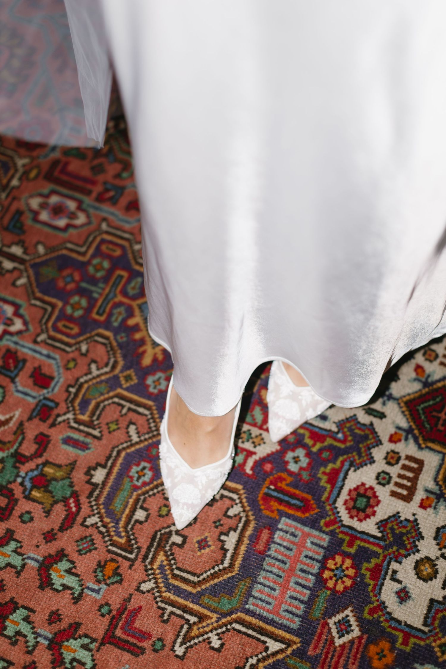White wedding dress hemline against vibrant traditional Persian carpet with ornate geometric patterns.