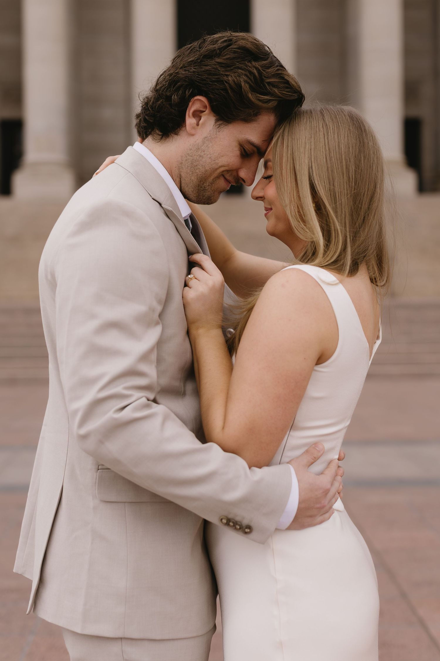 An intimate moment between a couple in formal wear standing before classical architecture.