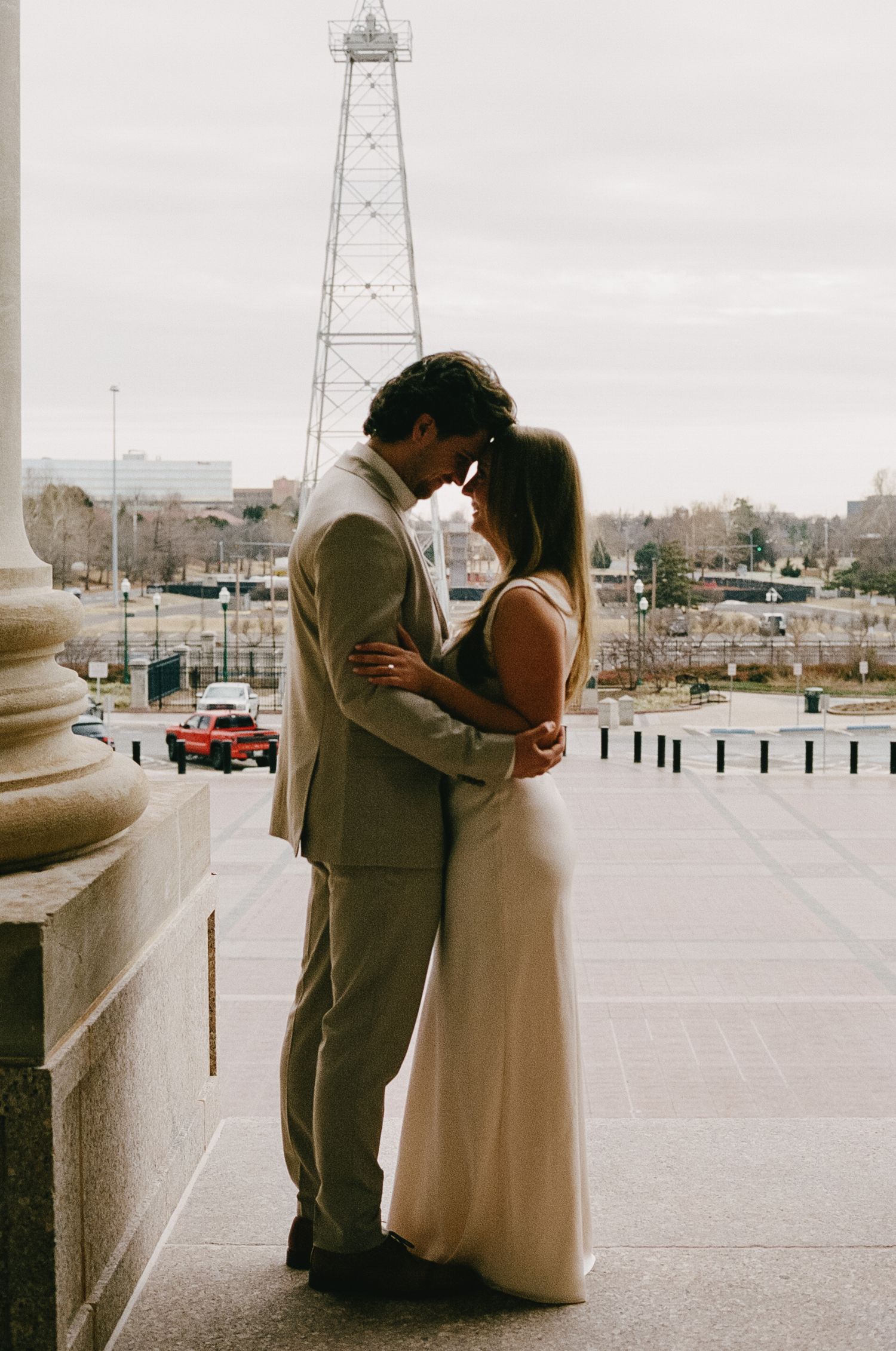 A couple in formal wear embracing with a lighthouse visible in the background.