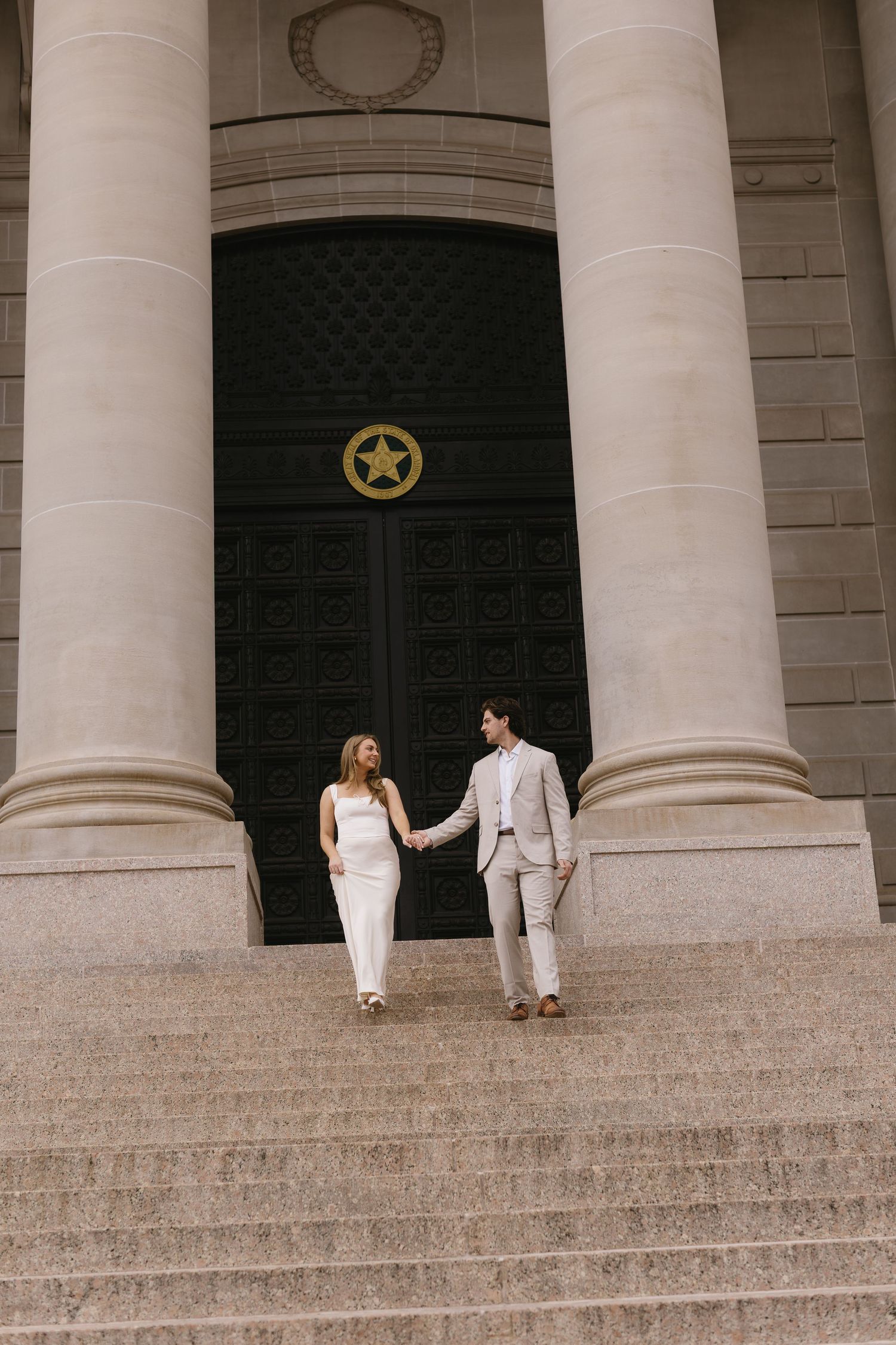 Two people in white outfits walk down grand stone steps of a historic building.