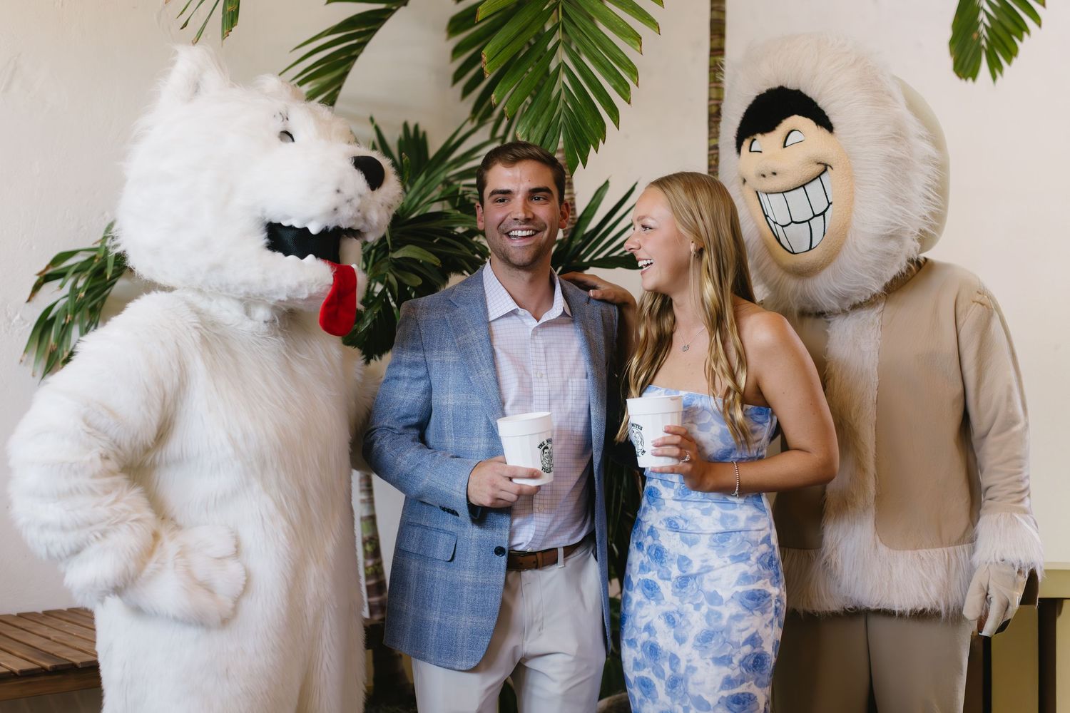 A group celebrates at an event with tropical decor and white brick walls.