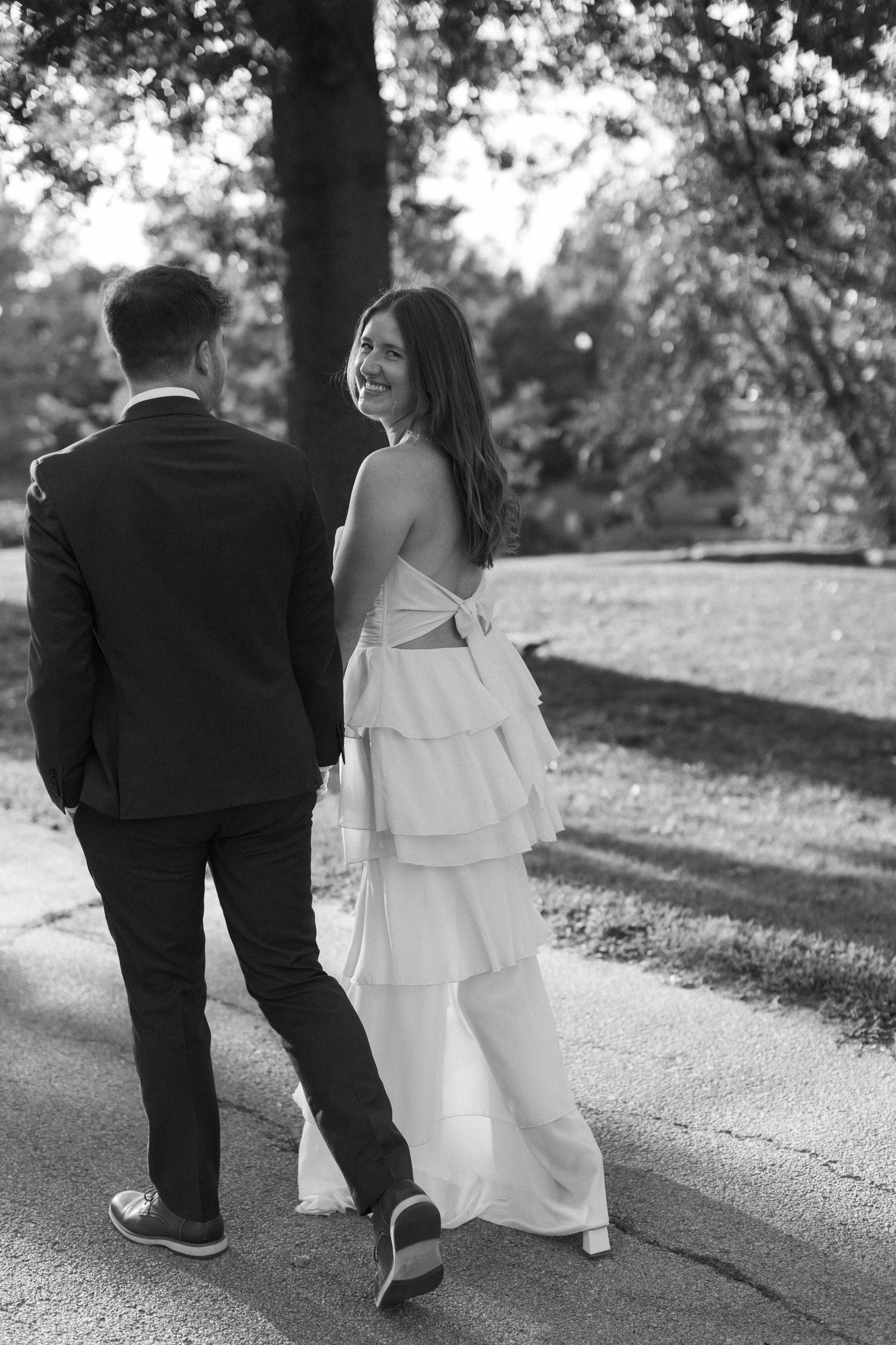 A couple in wedding attire walk together along a path in black and white.