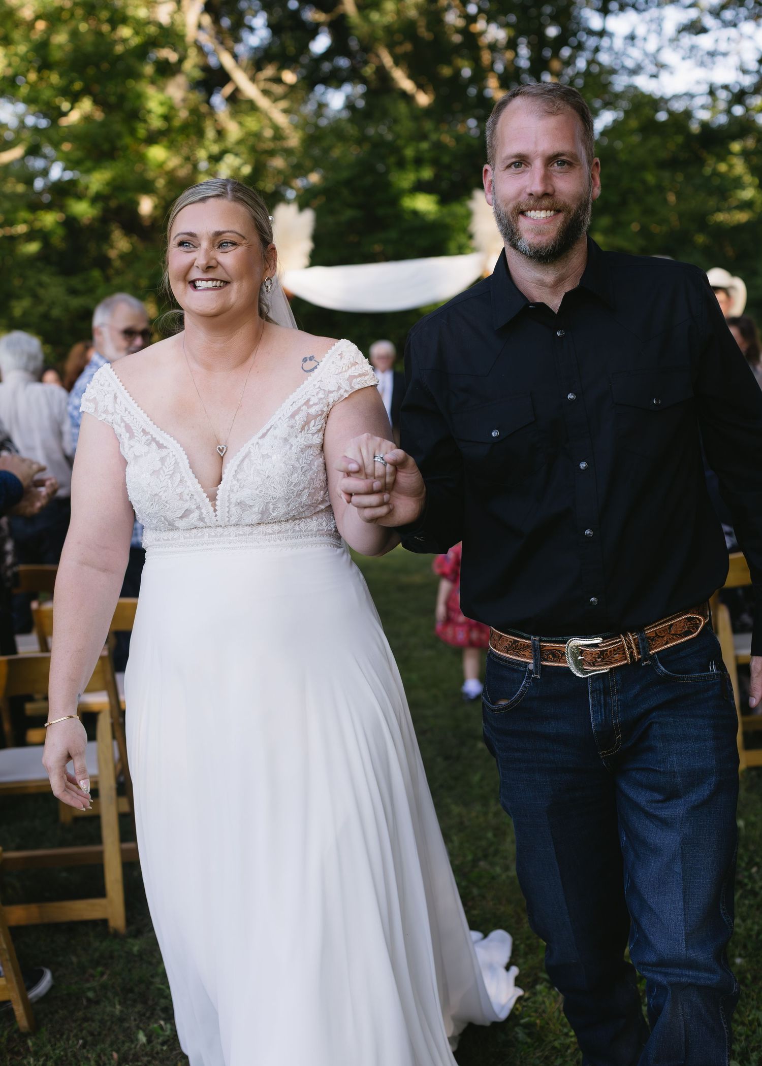 Wedding couple walks together on grass, bride in white dress and groom in dark attire.