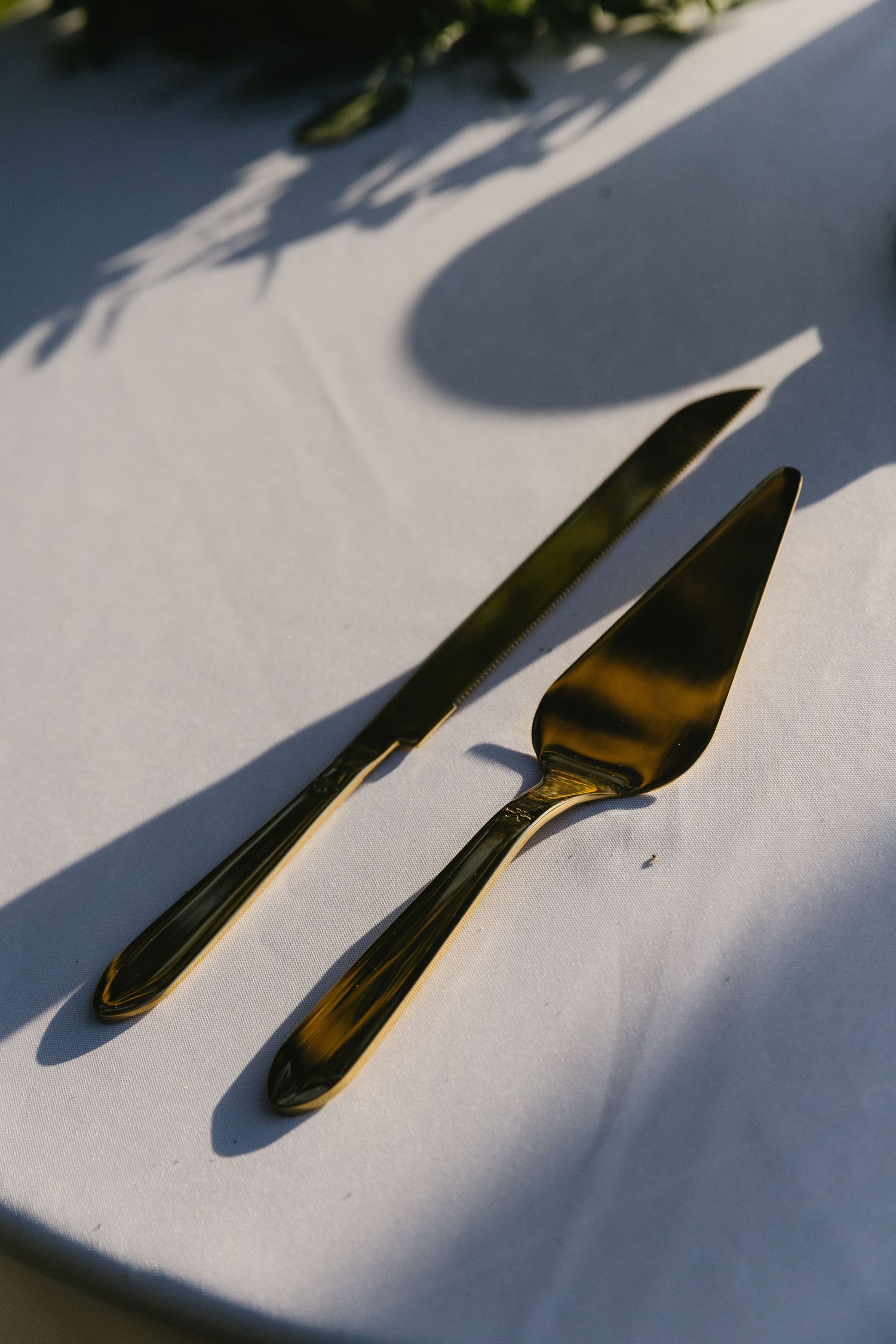 Two silver cake serving utensils casting shadows on white tablecloth.