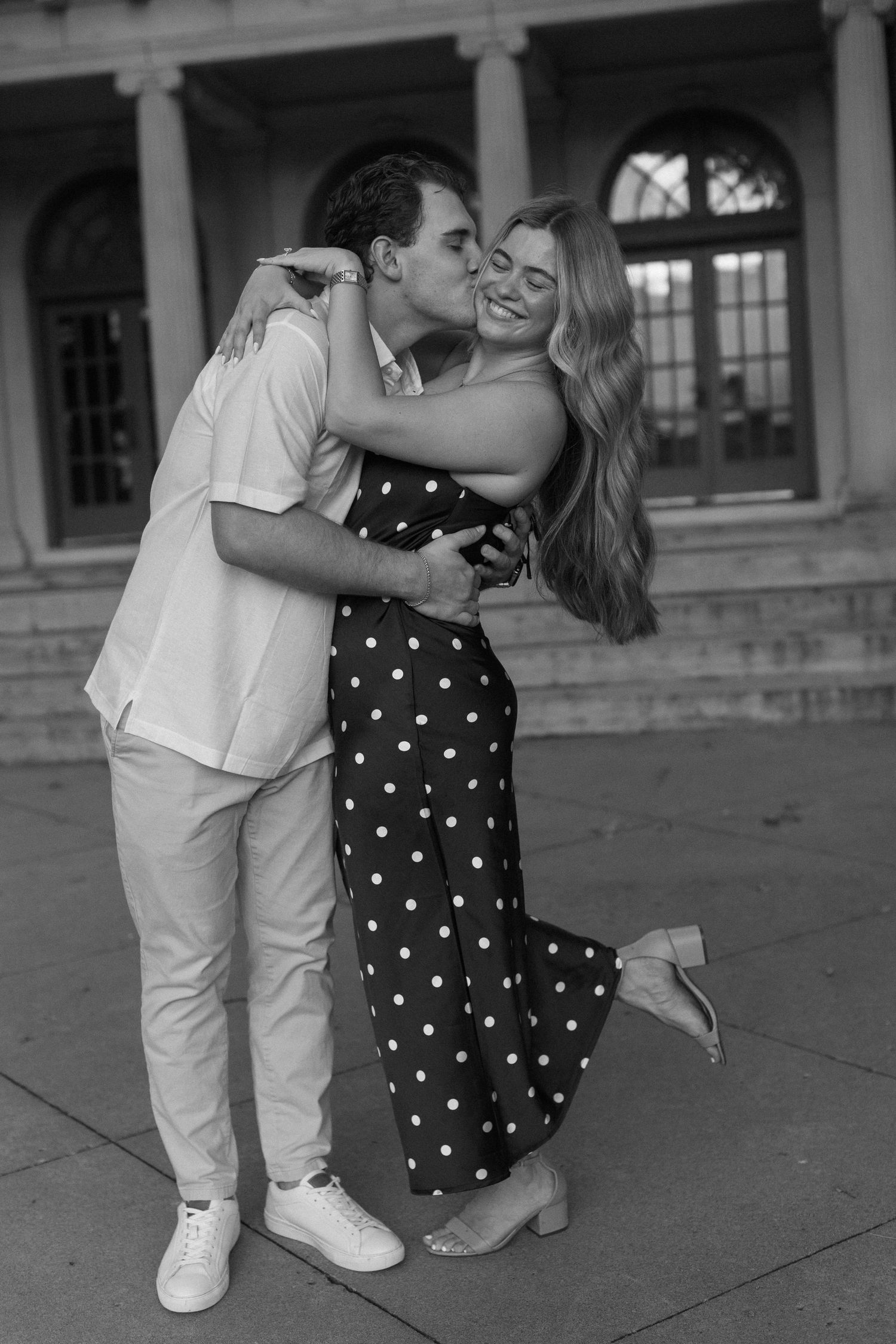 A couple dances playfully in an elegant outdoor setting with polka dot dress and white outfit.