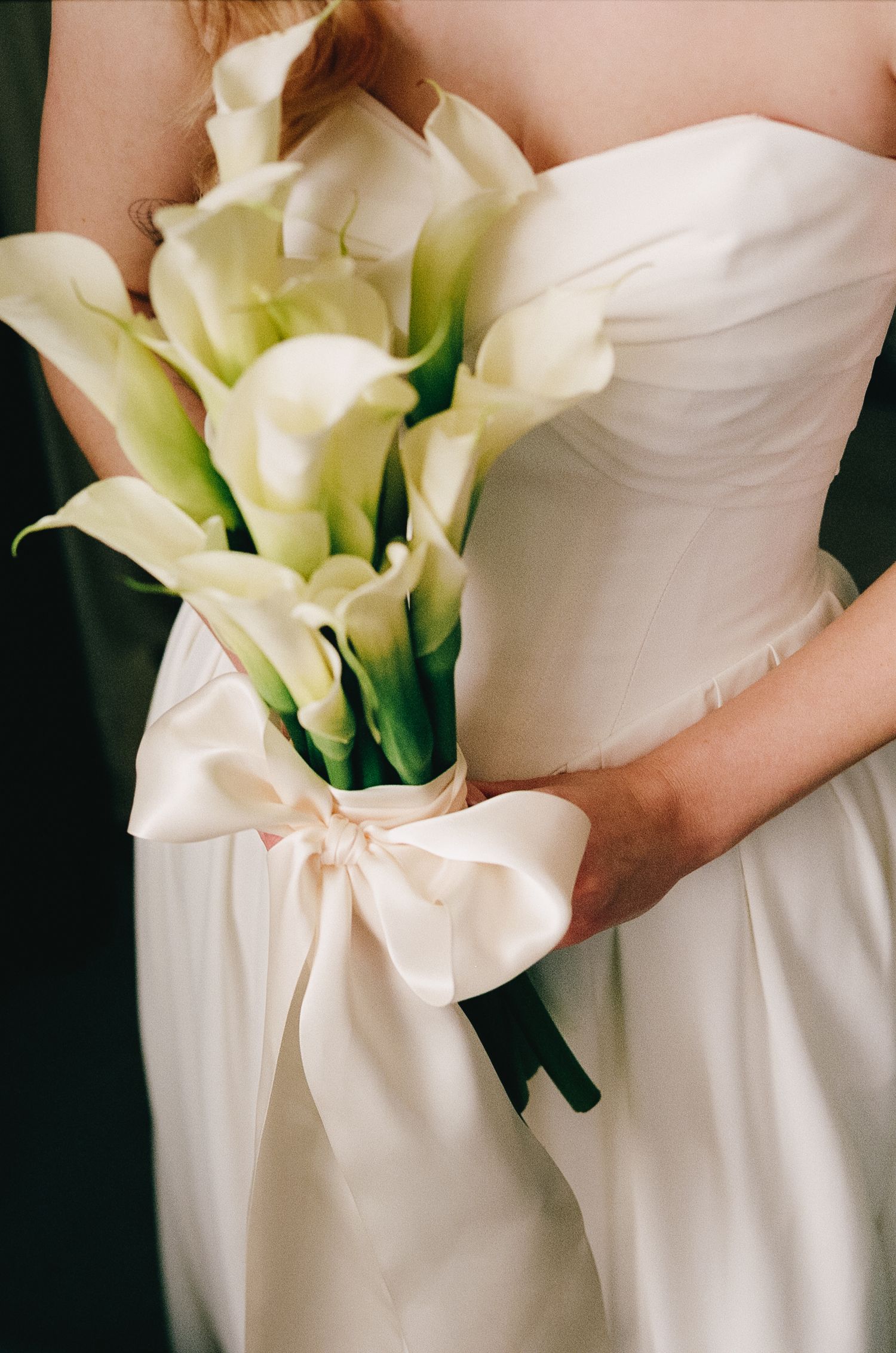 Elegant white wedding dress with calla lily bouquet detail.