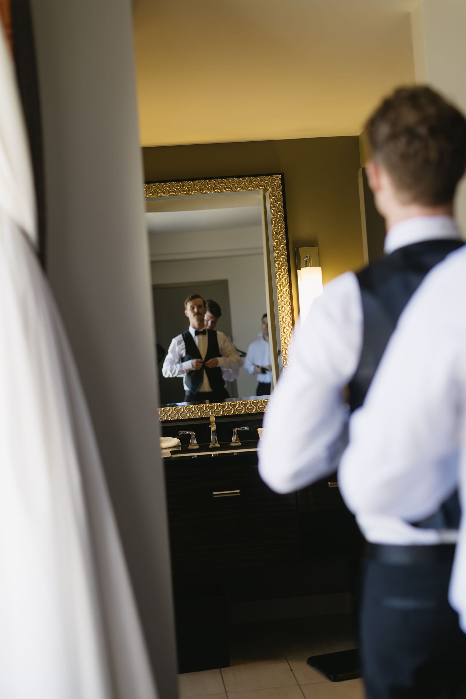 Person in formal attire adjusting their outfit in a bathroom mirror.