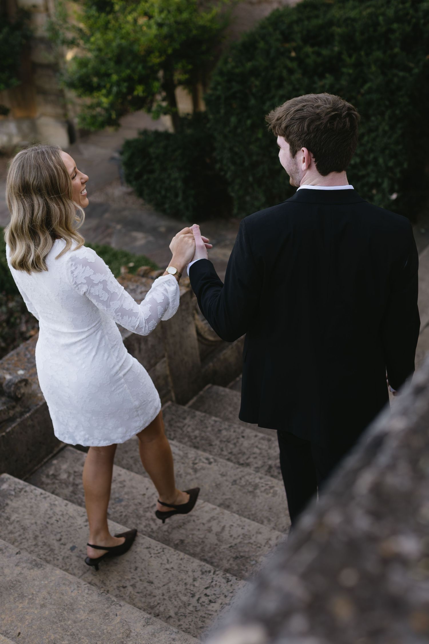 A couple playfully interacts on stone steps in an outdoor setting.
