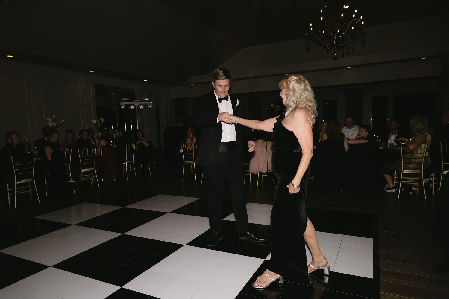 Guests dancing on black and white checkered dance floor during evening wedding reception.
