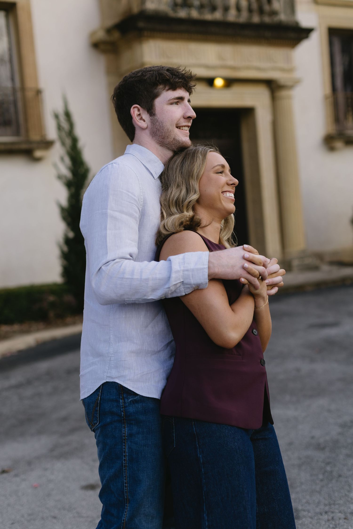 A tender moment captured between a couple in casual clothing against a stone building.