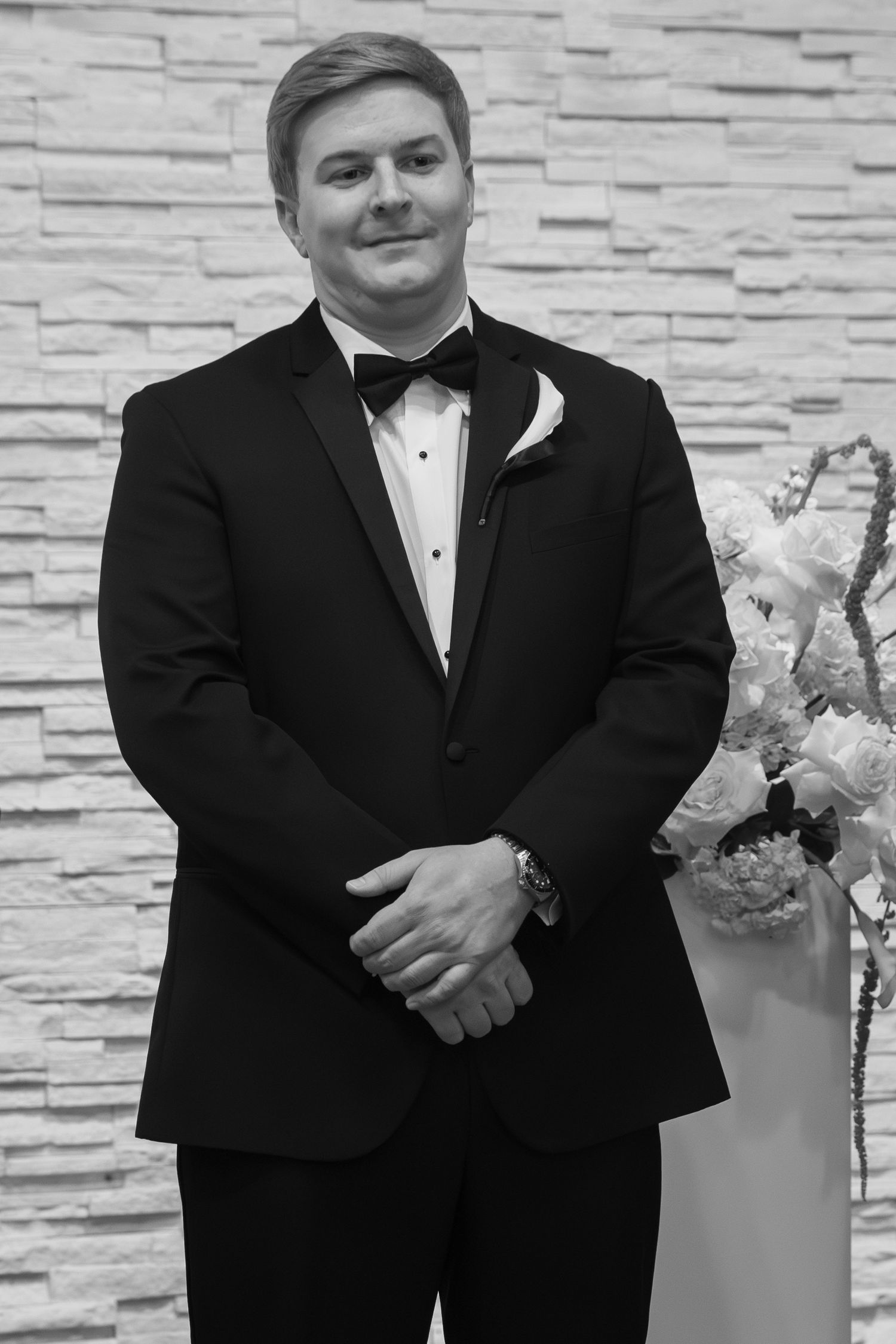 Black and white formal portrait against a stone wall background.