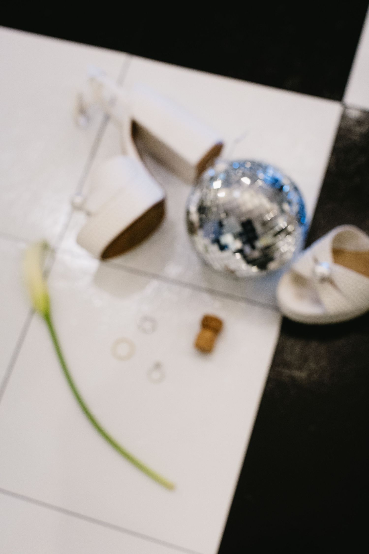 Elegant white heels with crystal details displayed next to wedding rings and disco ball on white surface.