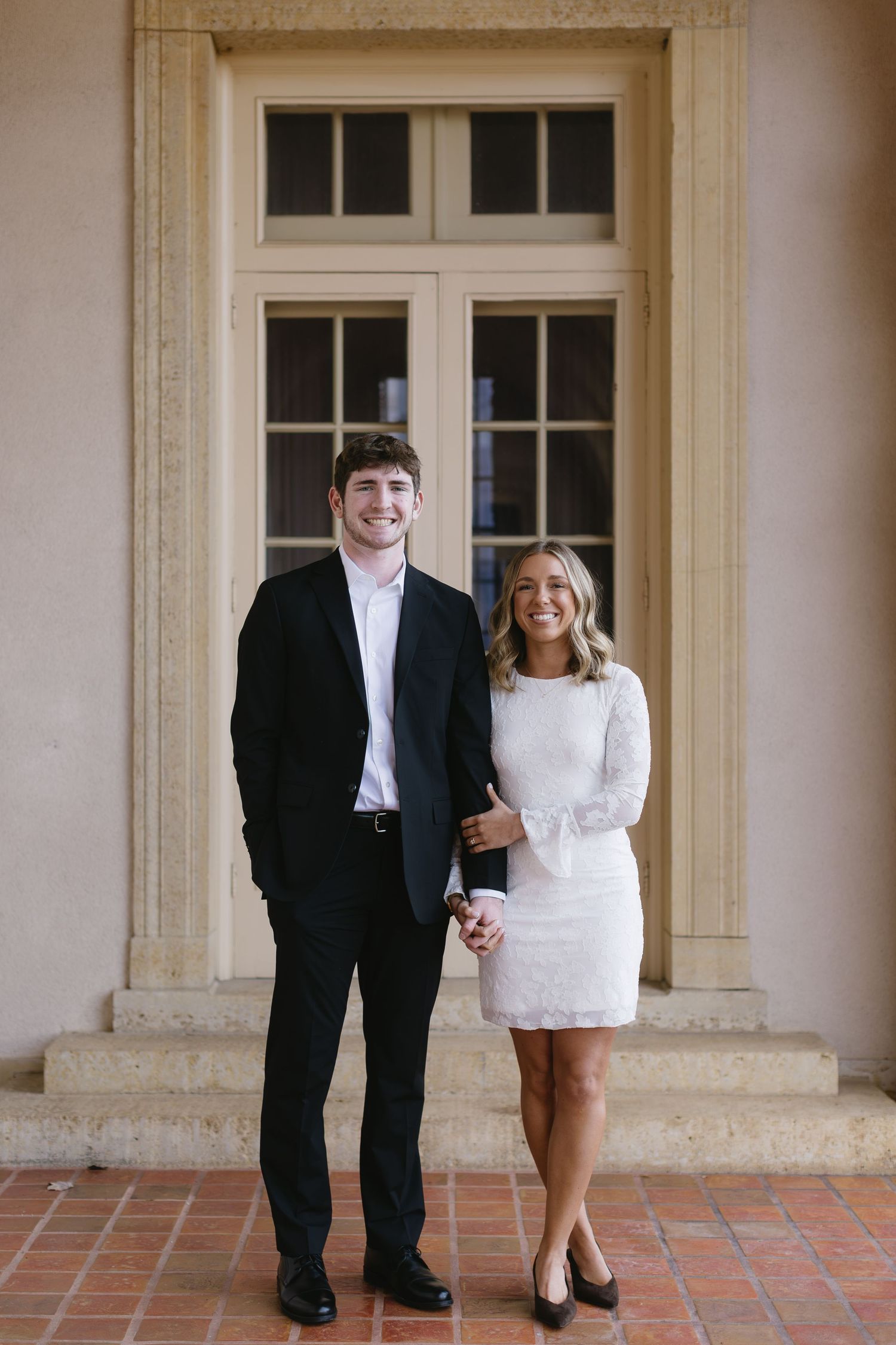 A couple poses for creative wedding photos showing just their legs and feet on a brick patio outside elegant doors.