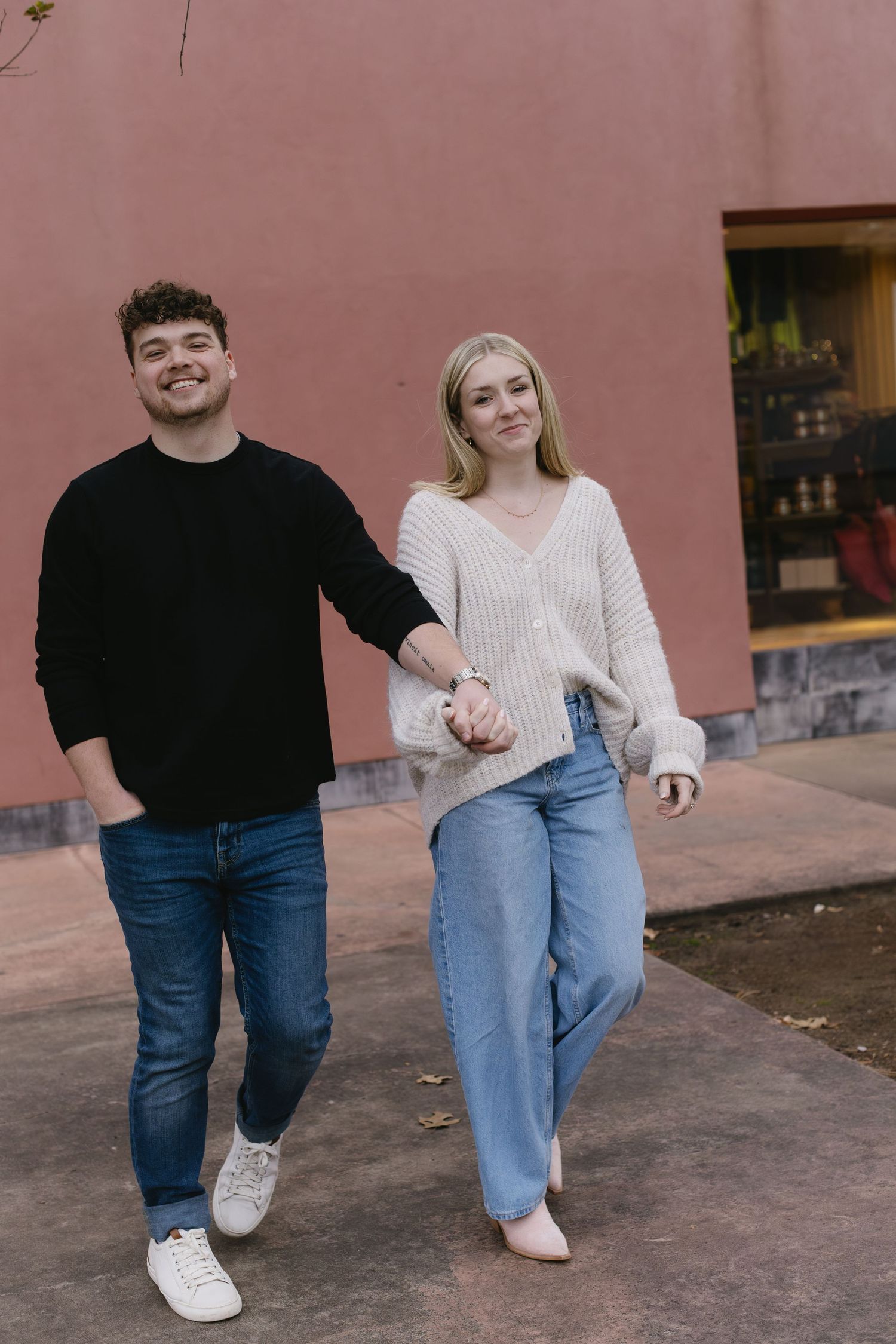 A couple taking synchronized steps together against a pink wall in matching casual attire.