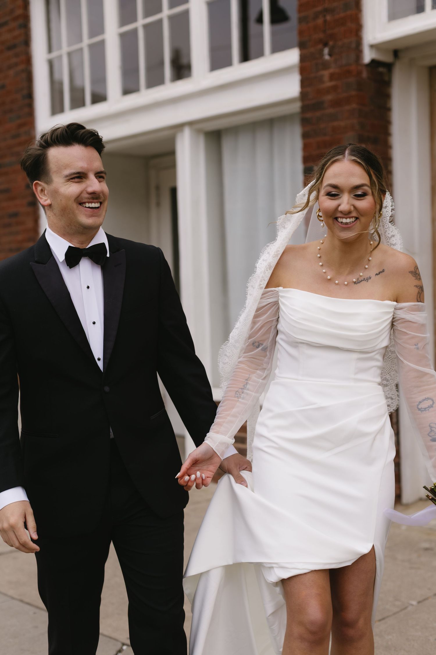 Bride and groom walking and laughing together outside a brick building.