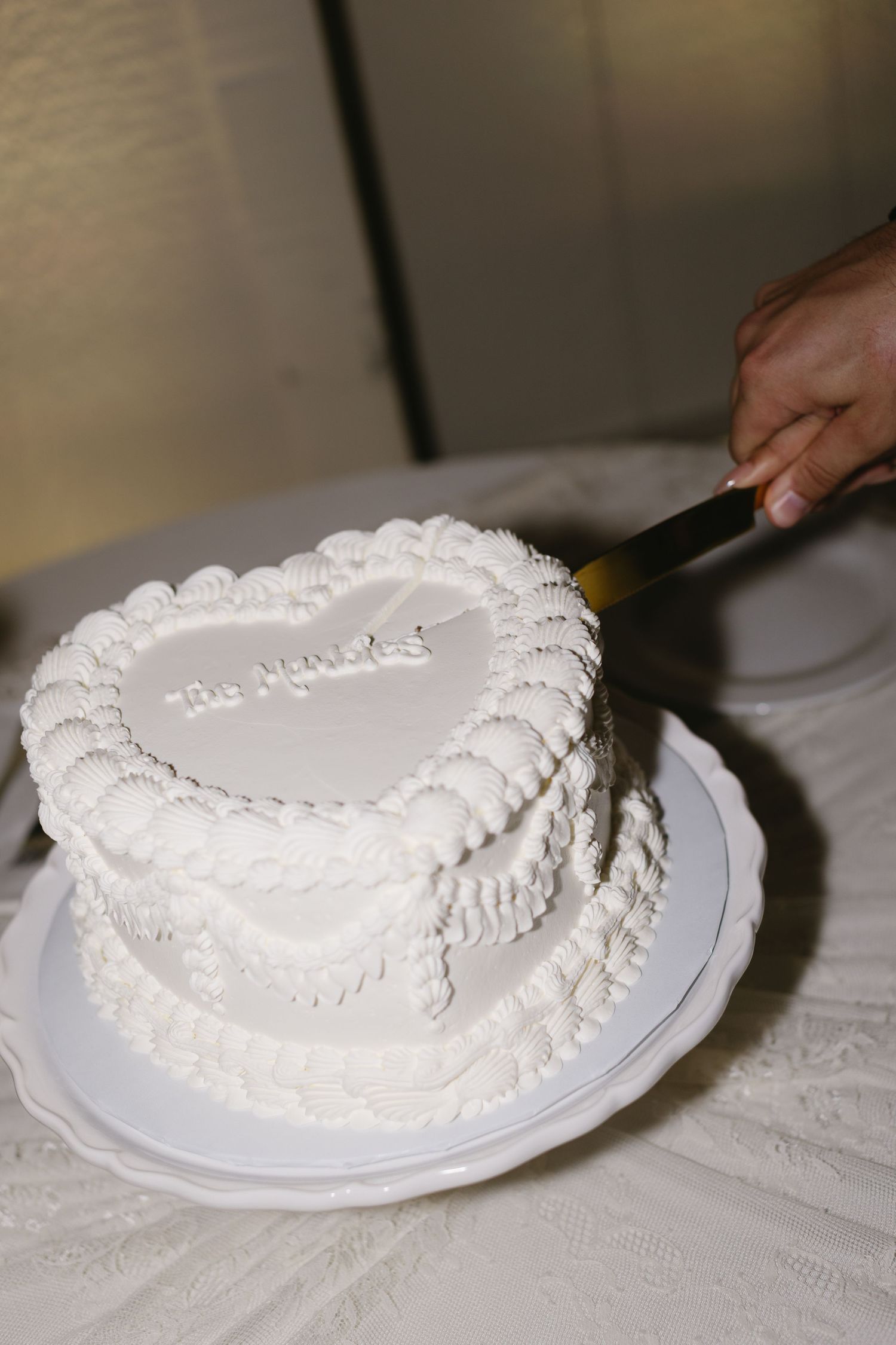 White heart-shaped wedding cake being cut on elegant white tablecloth.